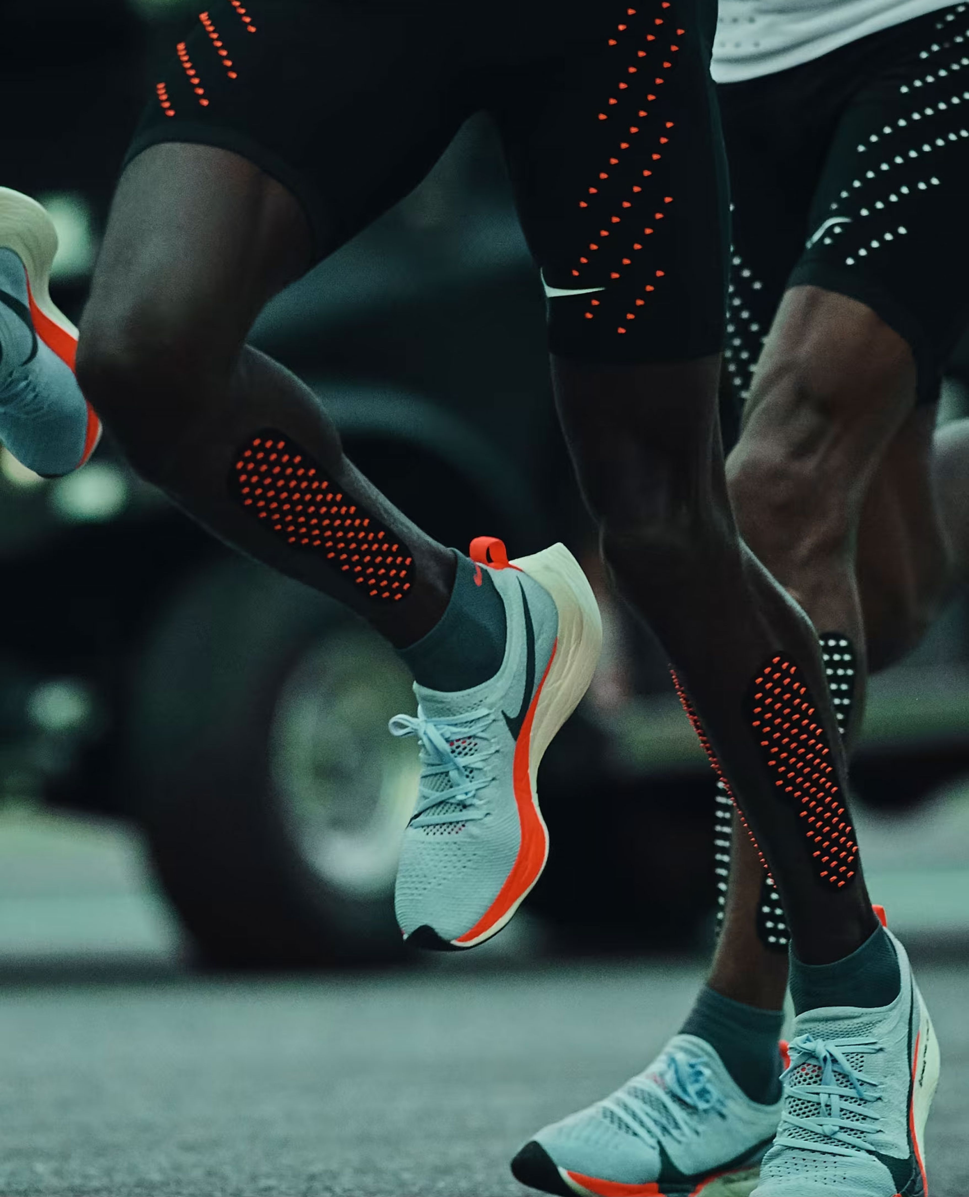 Close-up of a runner's legs wearing the Nike Zoom Air Vaporfly Elite racing shoes with orange midsole and Nike Swoosh.