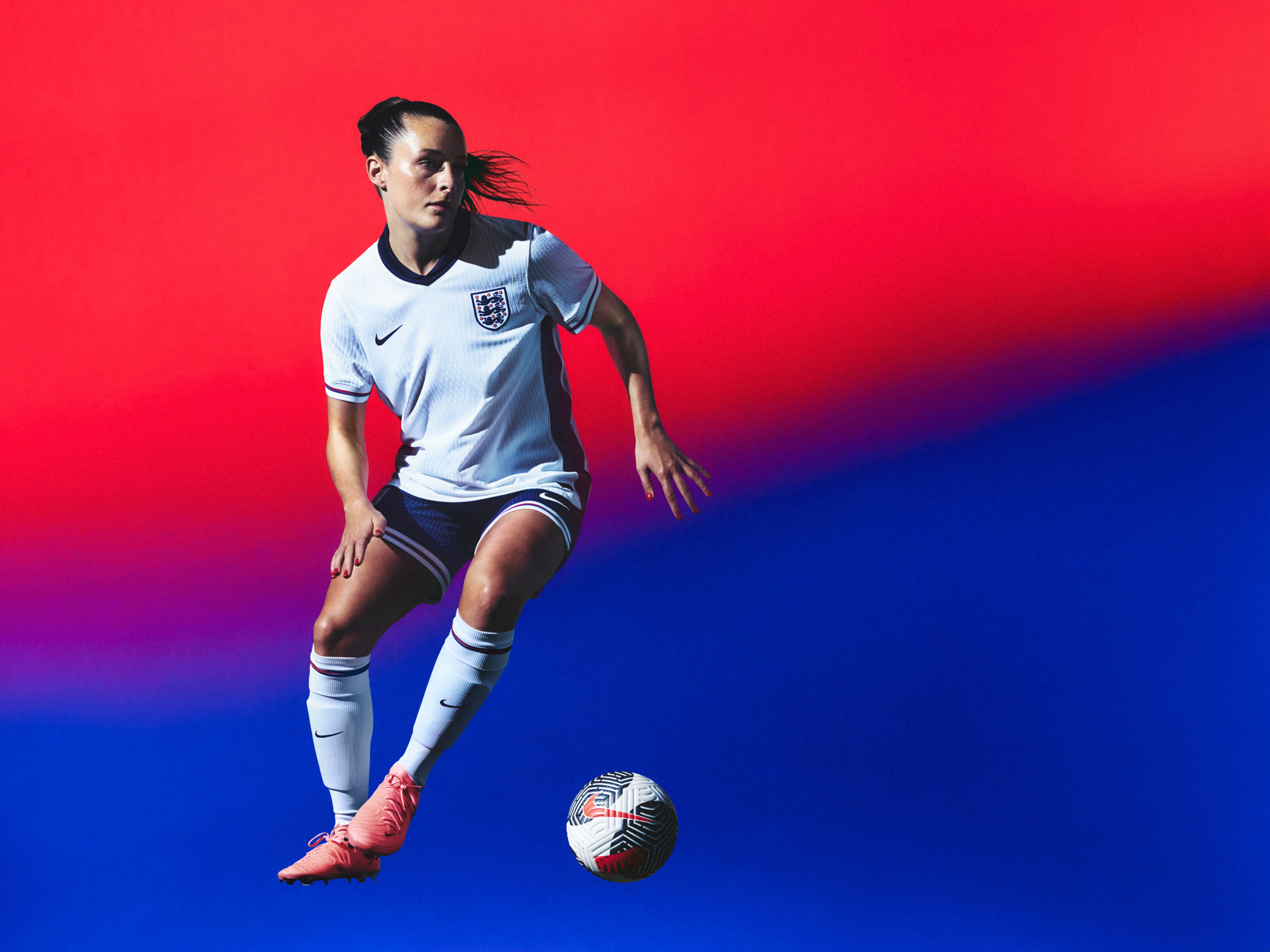 Athlete in a mid-kicking pose wearing a white soccer jersey with a navy blue collar and sides and red, white, and blue trim on the cuffs, as well as navy blue shorts with matching trim, each with a Nike swoosh and team logo on the chest and legs. They are also wearing white socks with matching trim.