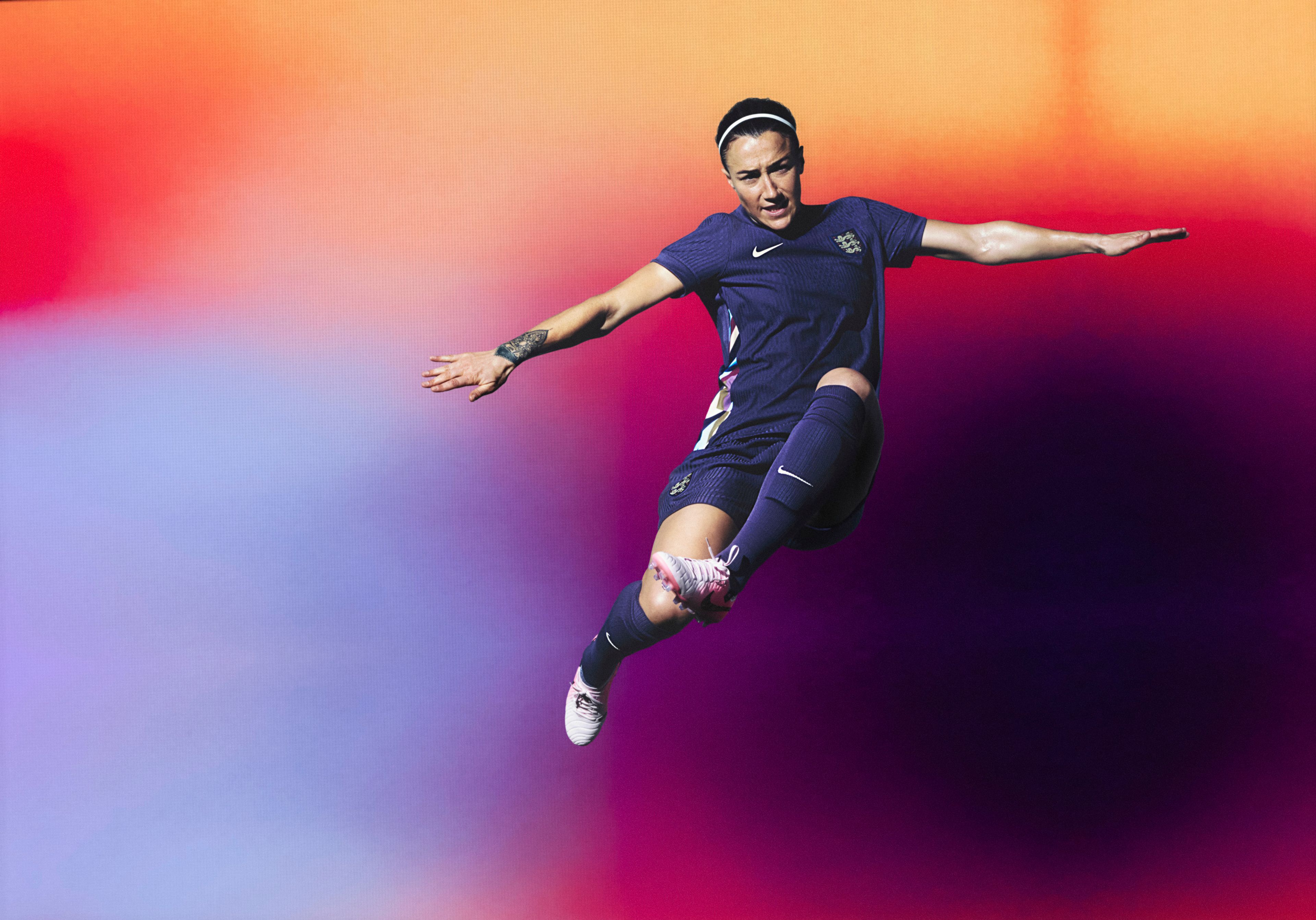 Athlete in a flying kicking pose wearing a navy blue soccer jersey with a colorful stripe pattern on the sides, as well as matching navy blue shorts, each with a Nike swoosh and team logo on the chest and legs. They are also wearing matching navy blue socks.
