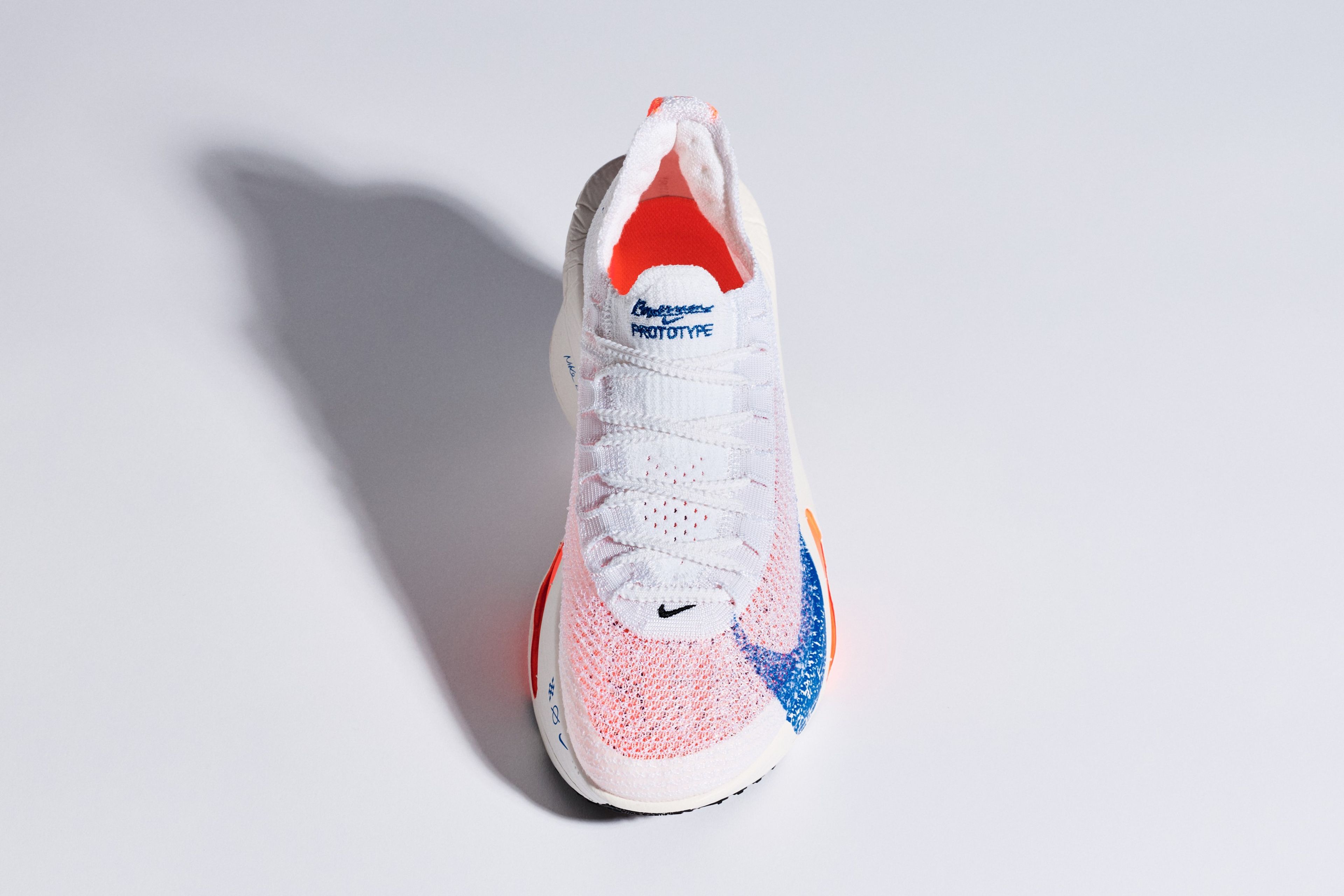 Top-down view of a Nike Alphafly 3 prototype running shoe in white with blue and orange accents on a light grey background.