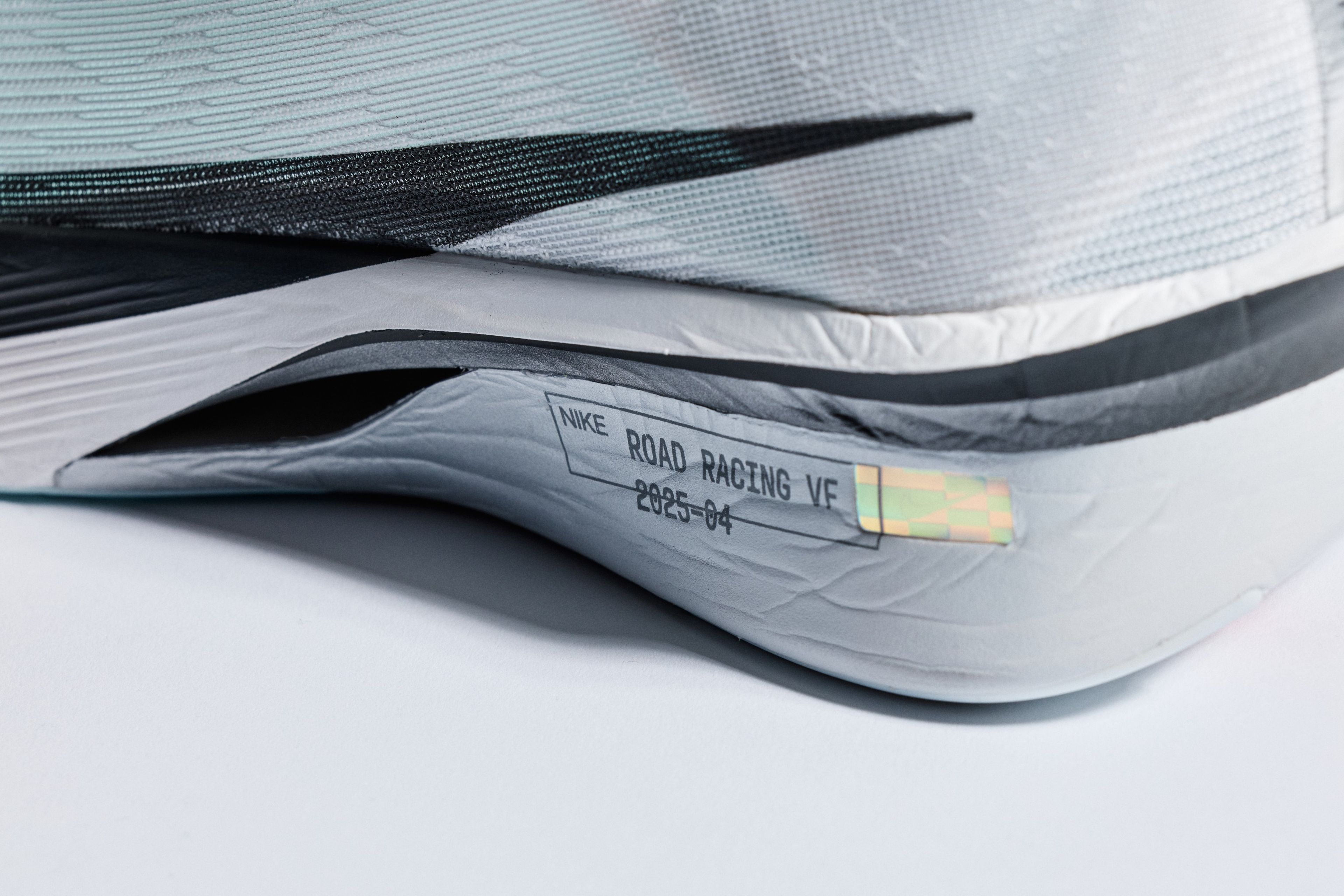 Close-up of Nike Vaporfly 4 stamped with 2025-04 and a holographic label, gray mesh upper and black Swoosh visible above.