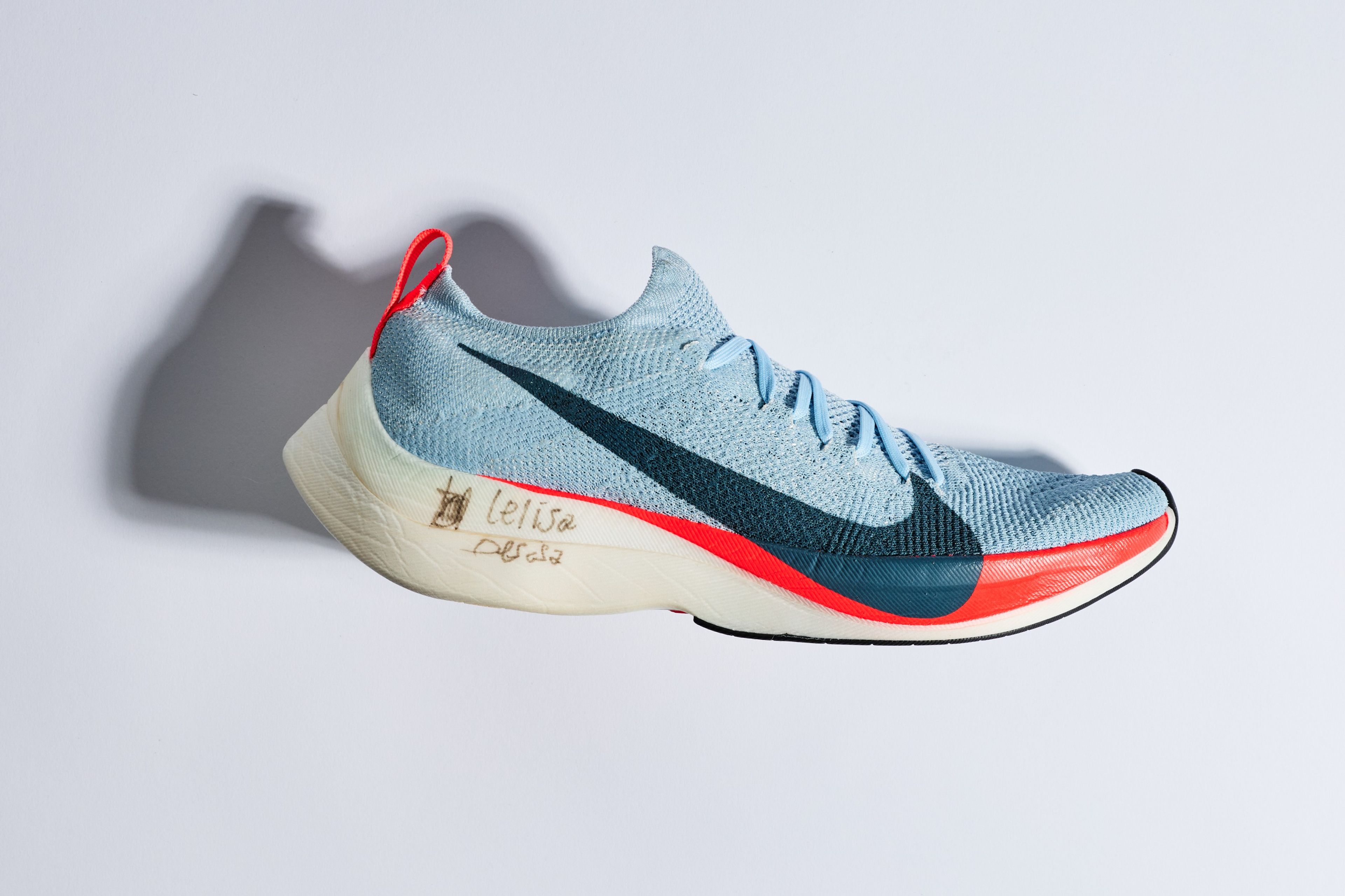 A light blue Nike Zoom Vaporfly Elite running shoe with dark Swoosh, red accents, and handwritten signature on the midsole, displayed against a clean white background.