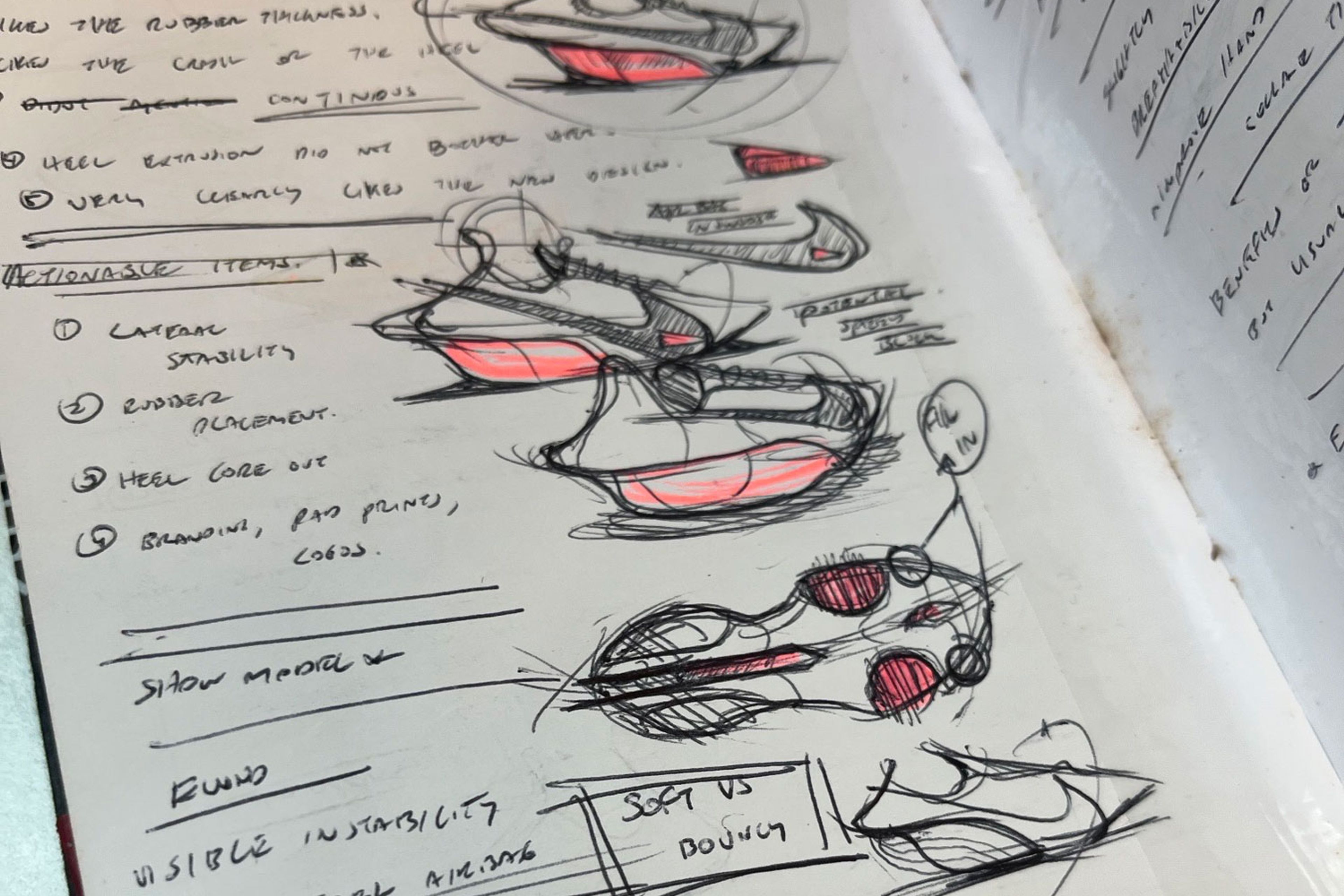 Hand-drawn Nike running shoe concept sketches in a design notebook with pink accent colorway, annotated with notes on lateral stability, heel core, rubber placement, and soft vs bouncy cushioning.