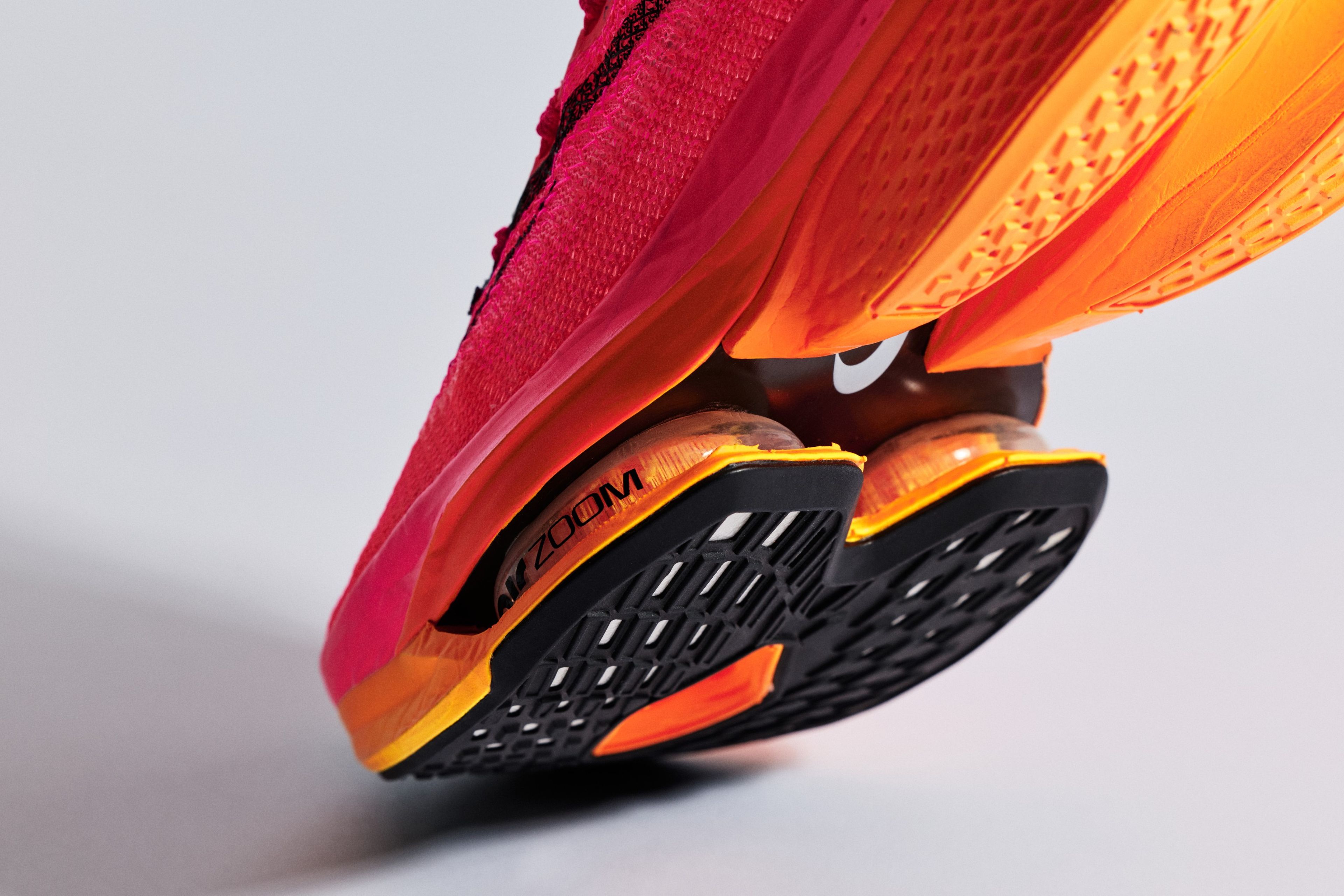 Close-up of the Nike Air Zoom Alphafly NEXT% 2 running shoe showing the visible Zoom Air units and orange-red gradient upper against a neutral background.