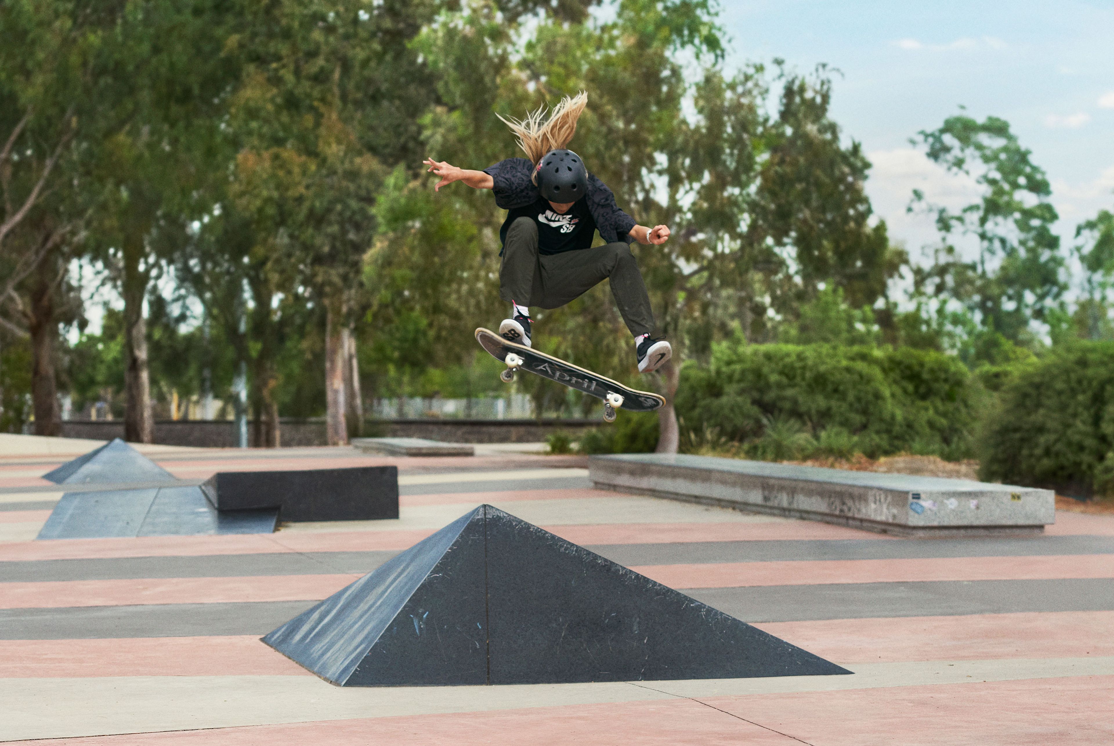 Male skateboarder doing a kick flip in the air with their skateboard at a skate park while wearing the Nike SB Day One's in black.