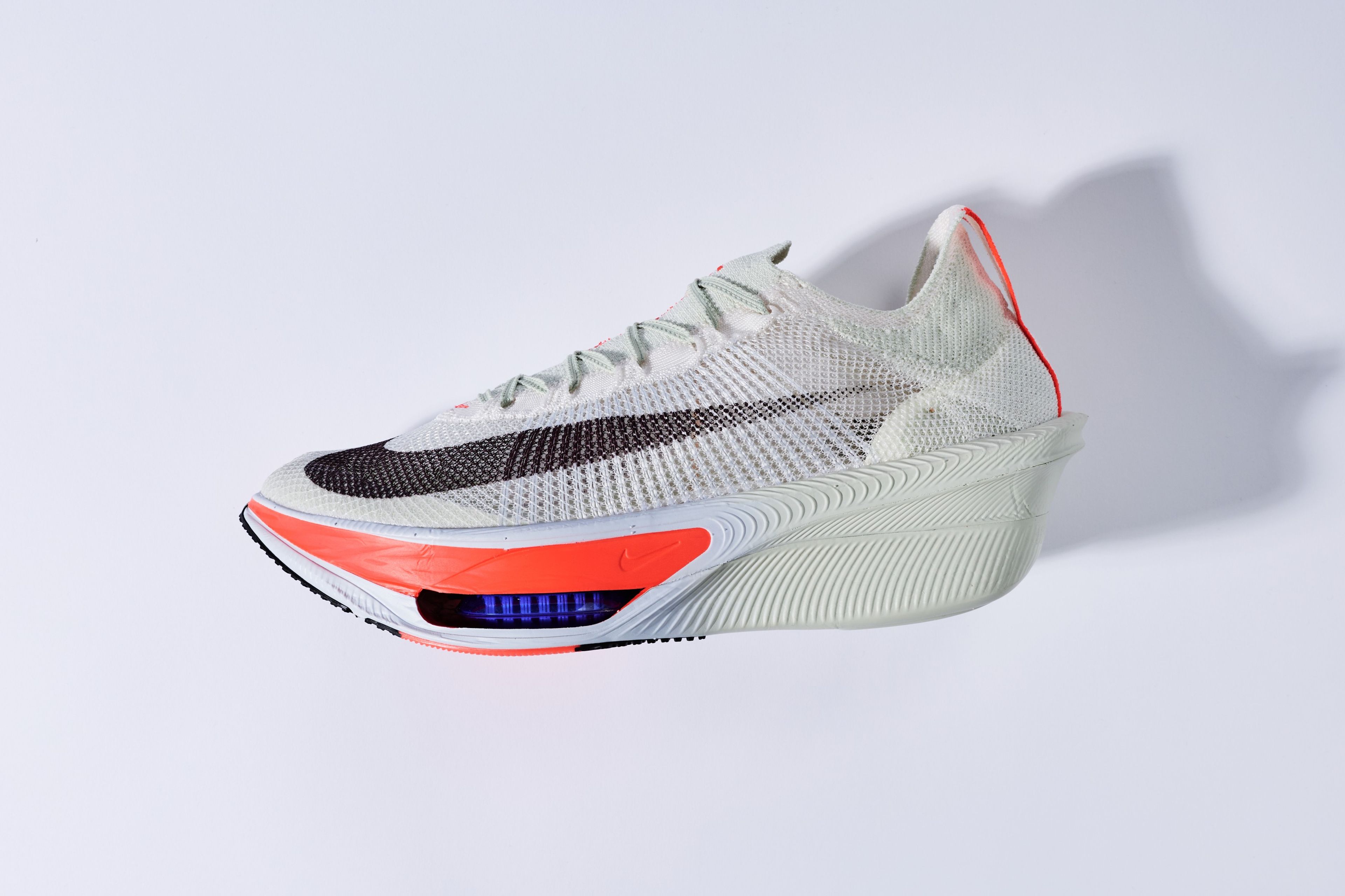 Nike Alphafly 4 running shoe in white with black Swoosh and bright orange accents, shown in profile against a clean grey background.