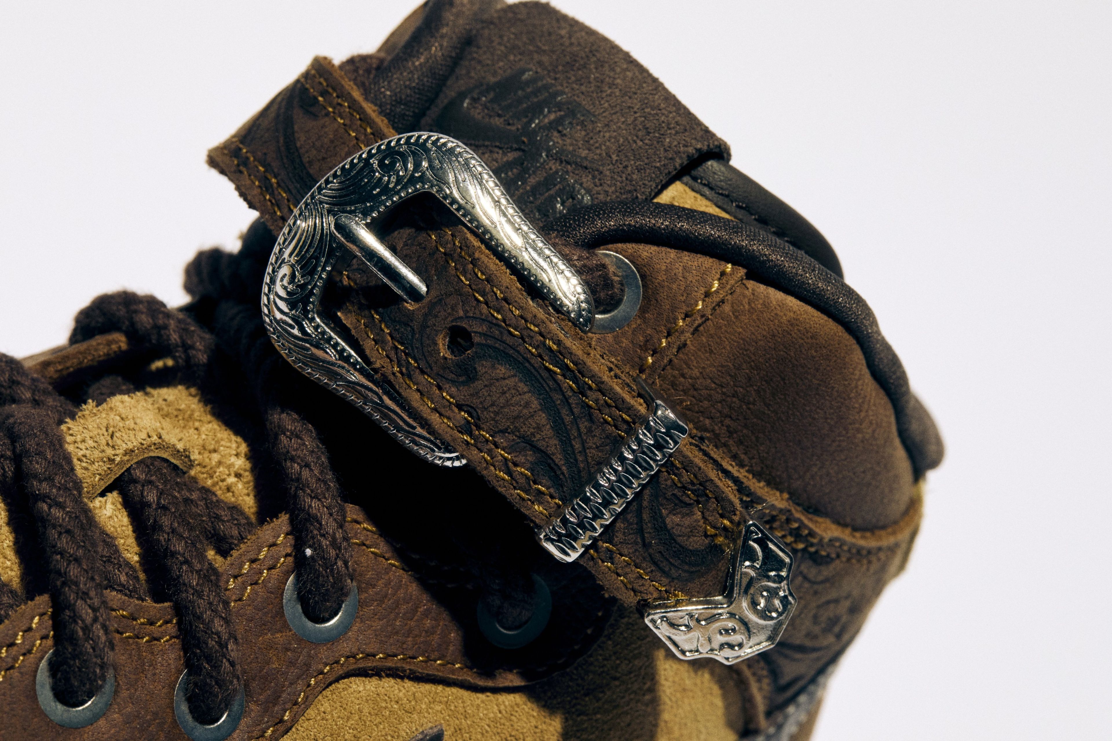 A silver pronged buckle and unique pattern debossed into the leather of Royce’s Nike Air Force 1 Mid.