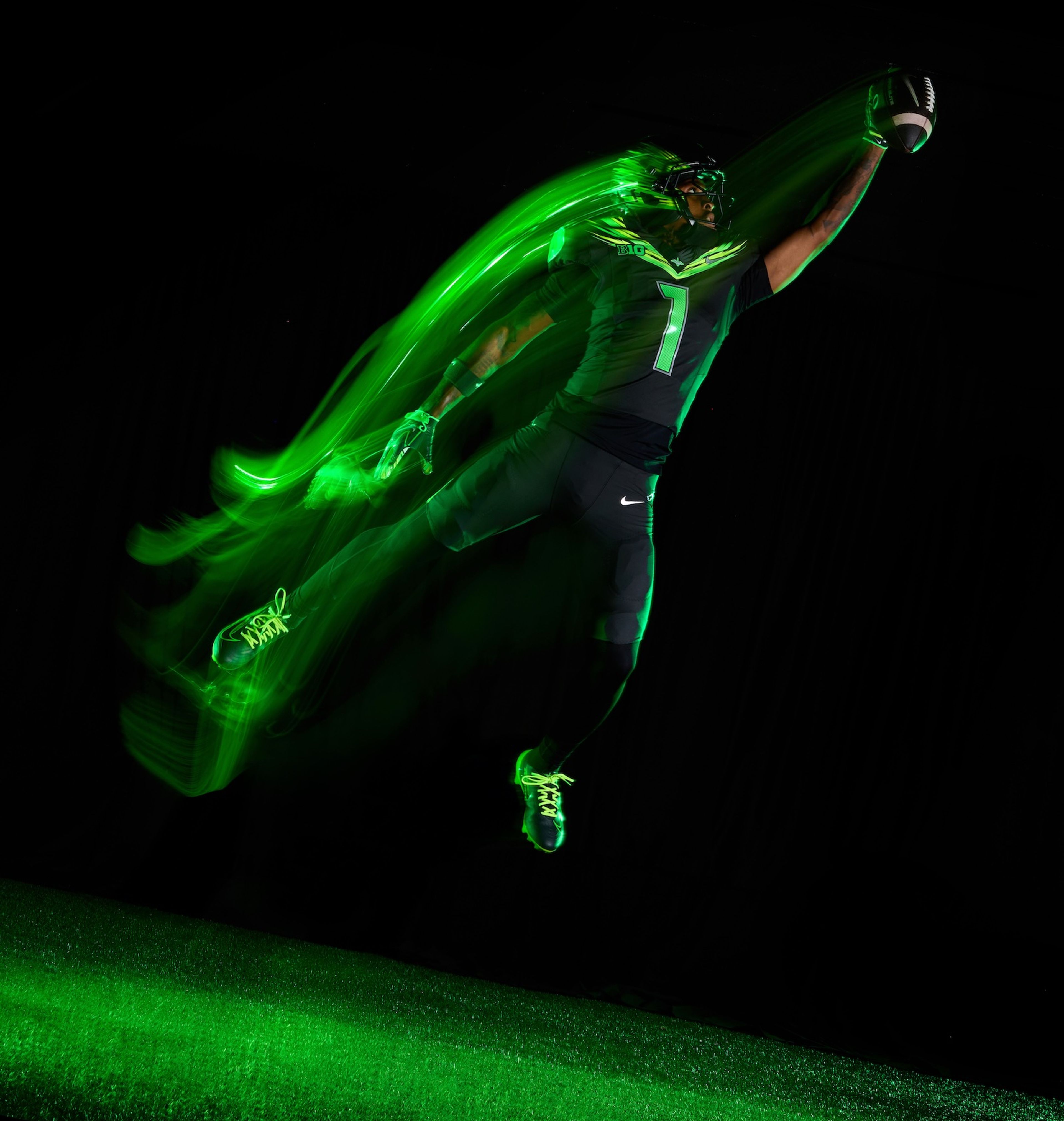 A football player in an Oregon Ducks uniform leaps to catch a football.