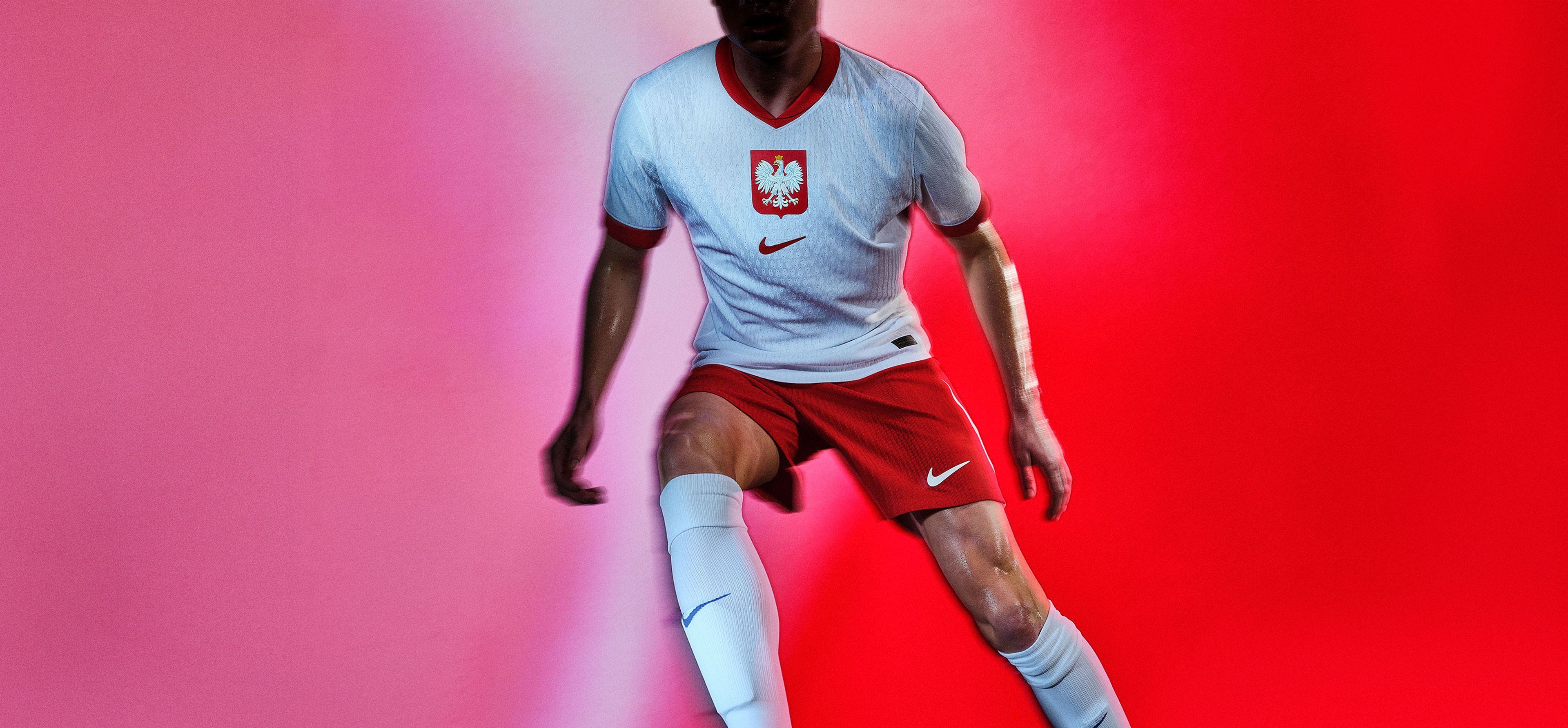 Athlete in a running pose wearing a white soccer jersey with a red collar and red cuffs, as well as matching red shorts, each with a Nike swoosh and team logo on the chest and legs.