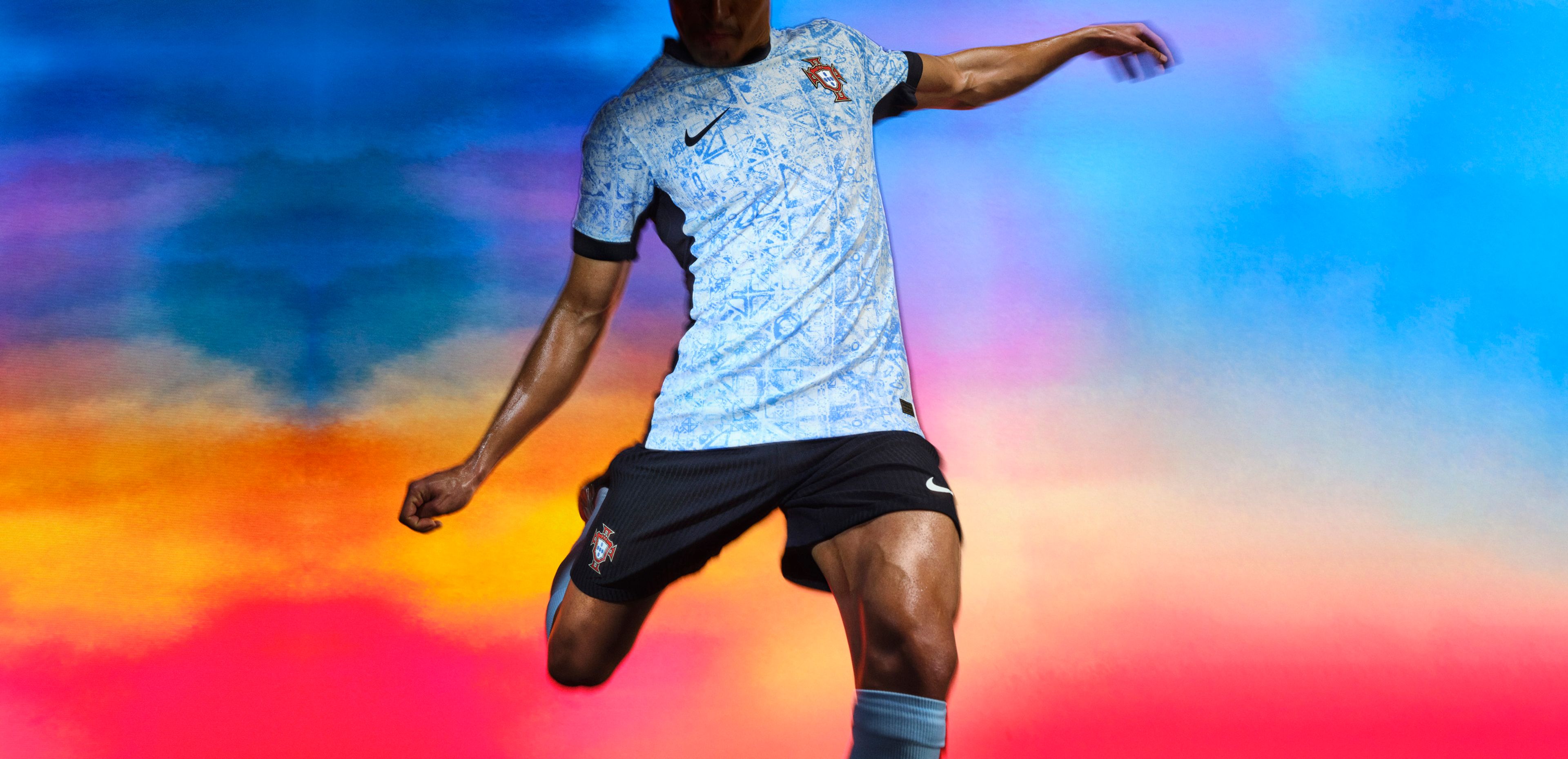 Athlete in a mid-kicking pose wearing a white soccer jersey with black sides, a black collar, black cuffs, and a faded light blue triangle pattern, as well as matching black shorts, each with a Nike swoosh and team logo on the chest and legs.