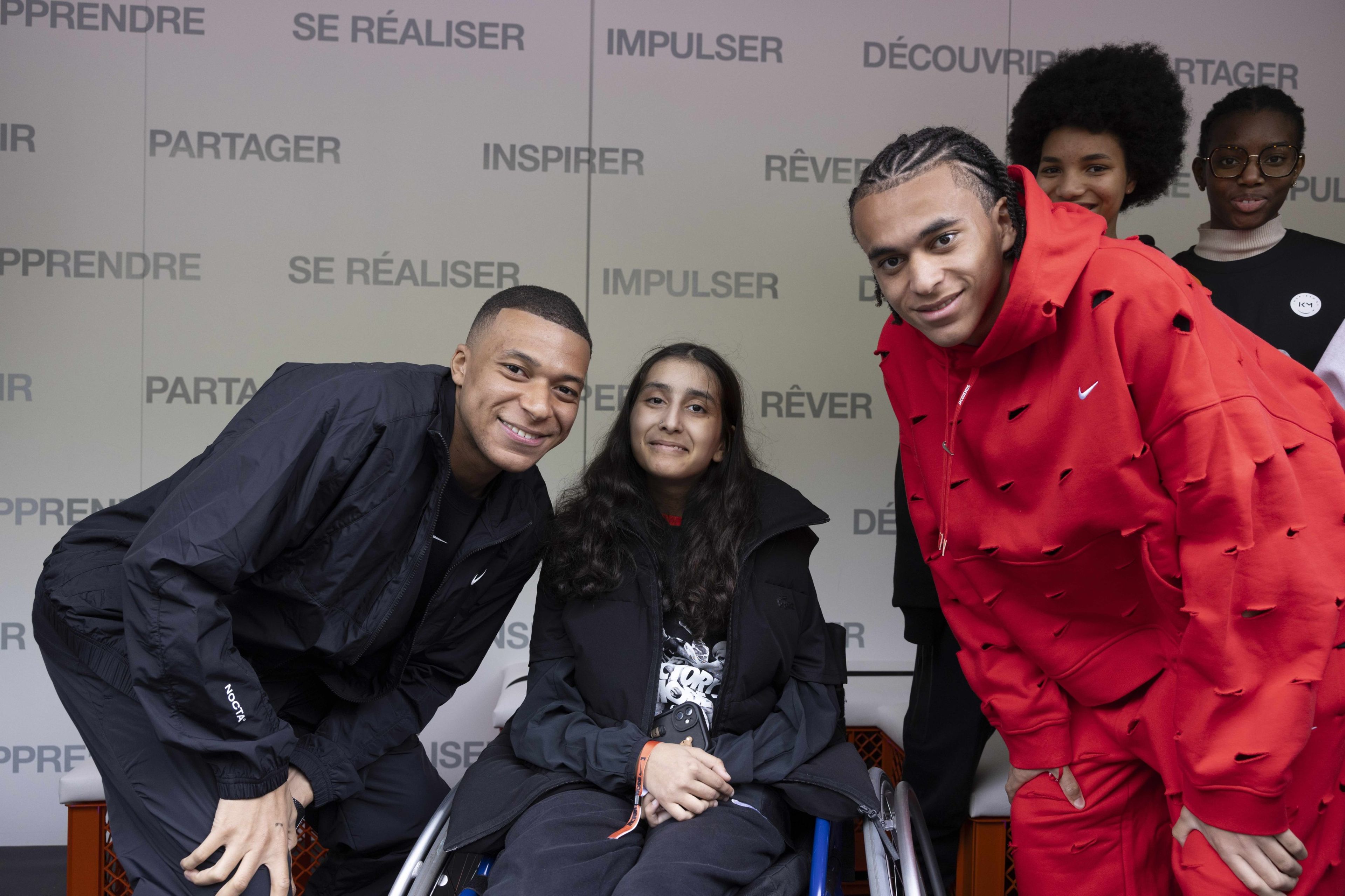 Kylian and Ethan Mbappe pose with a young athlete in a wheelchair, while other young athletes look on at the Victory Mode event in Paris, France.