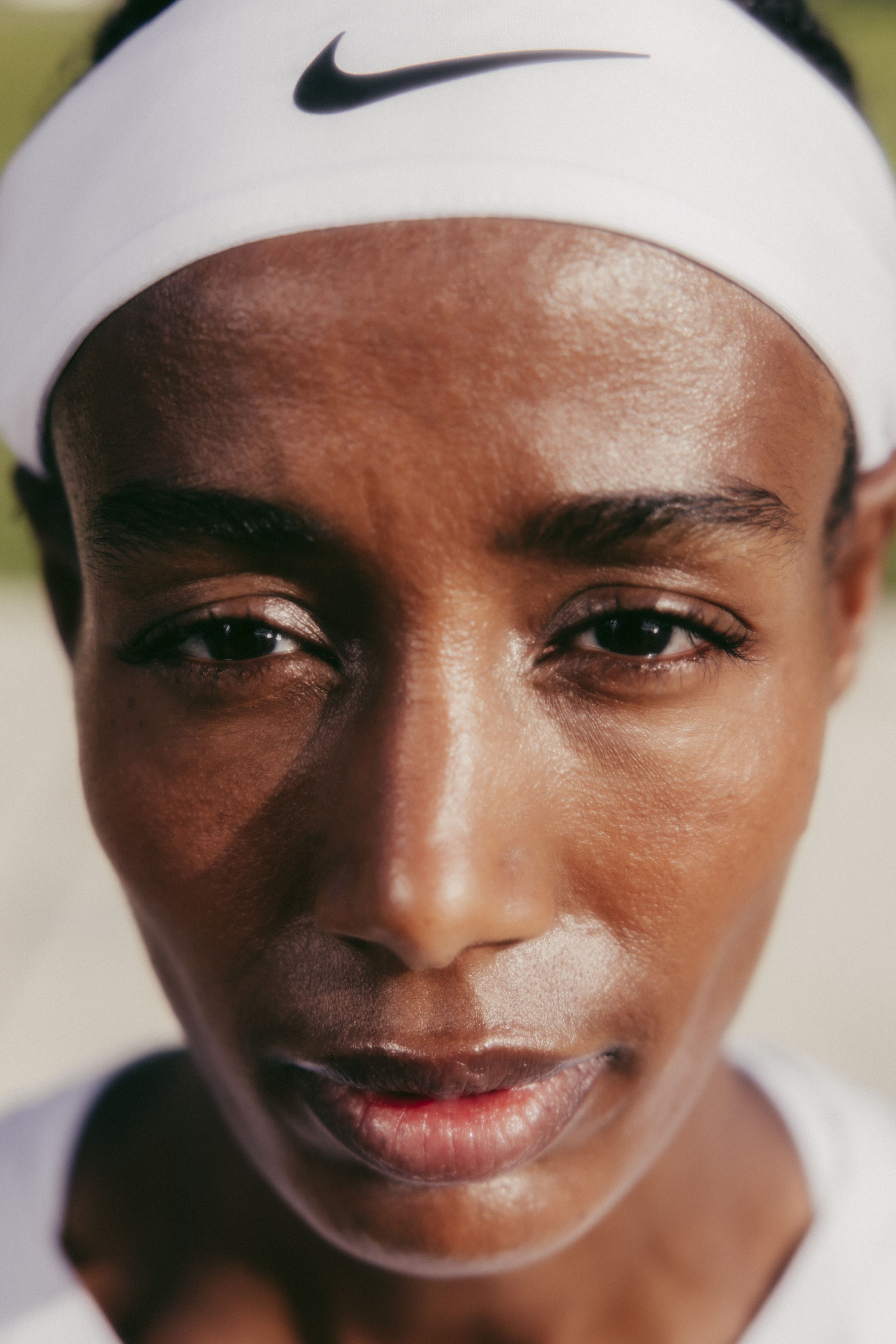 Close up head shot of Sifan Hassan wearing a white Nike headband with a black Swoosh. Sifan's face is partially in shadow.