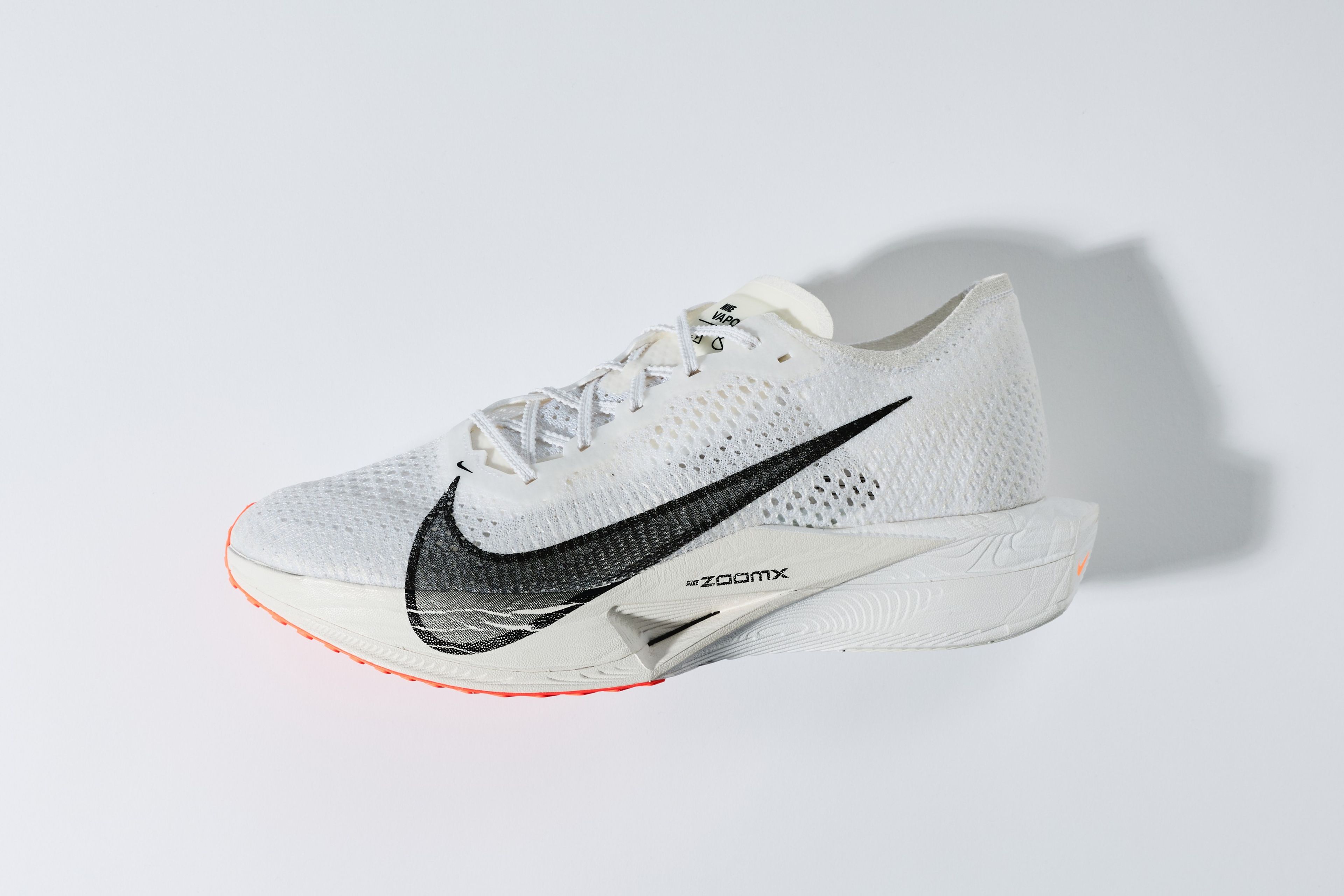 Nike Vaporfly 3 running shoe with white Flyknit upper, black Nike Swoosh, ZoomX midsole label, and orange outsole on white background.