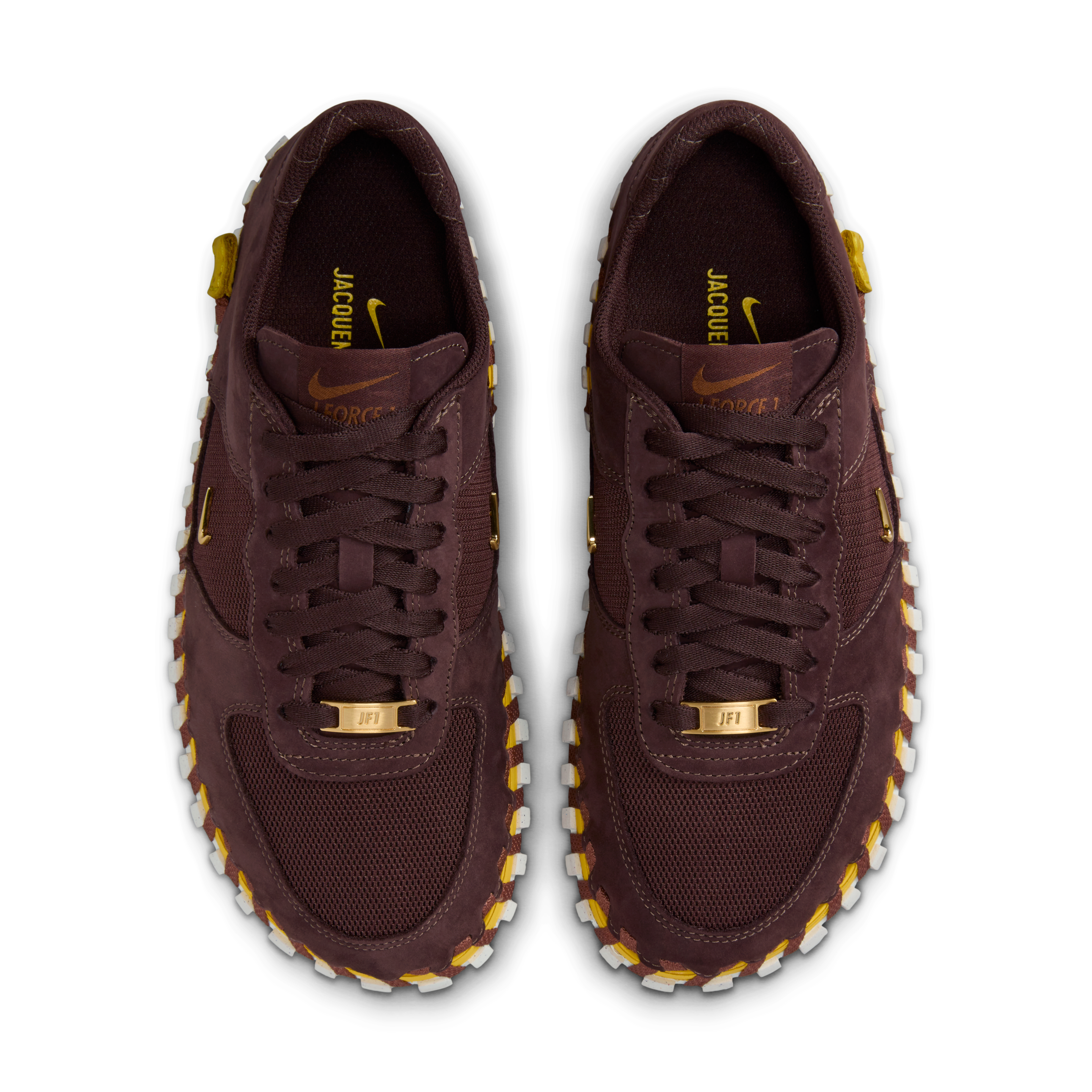 Overhead view of a pair of Nike x Jacquemus J Force 1 Low LX SP with Earth brown upper, tour yellow midsole, and white sole. Includes, brown laces and AF1 lace tags in gold metal. There are small metallic gold Swooshes on the shoes sides. The pair floats on a black background.