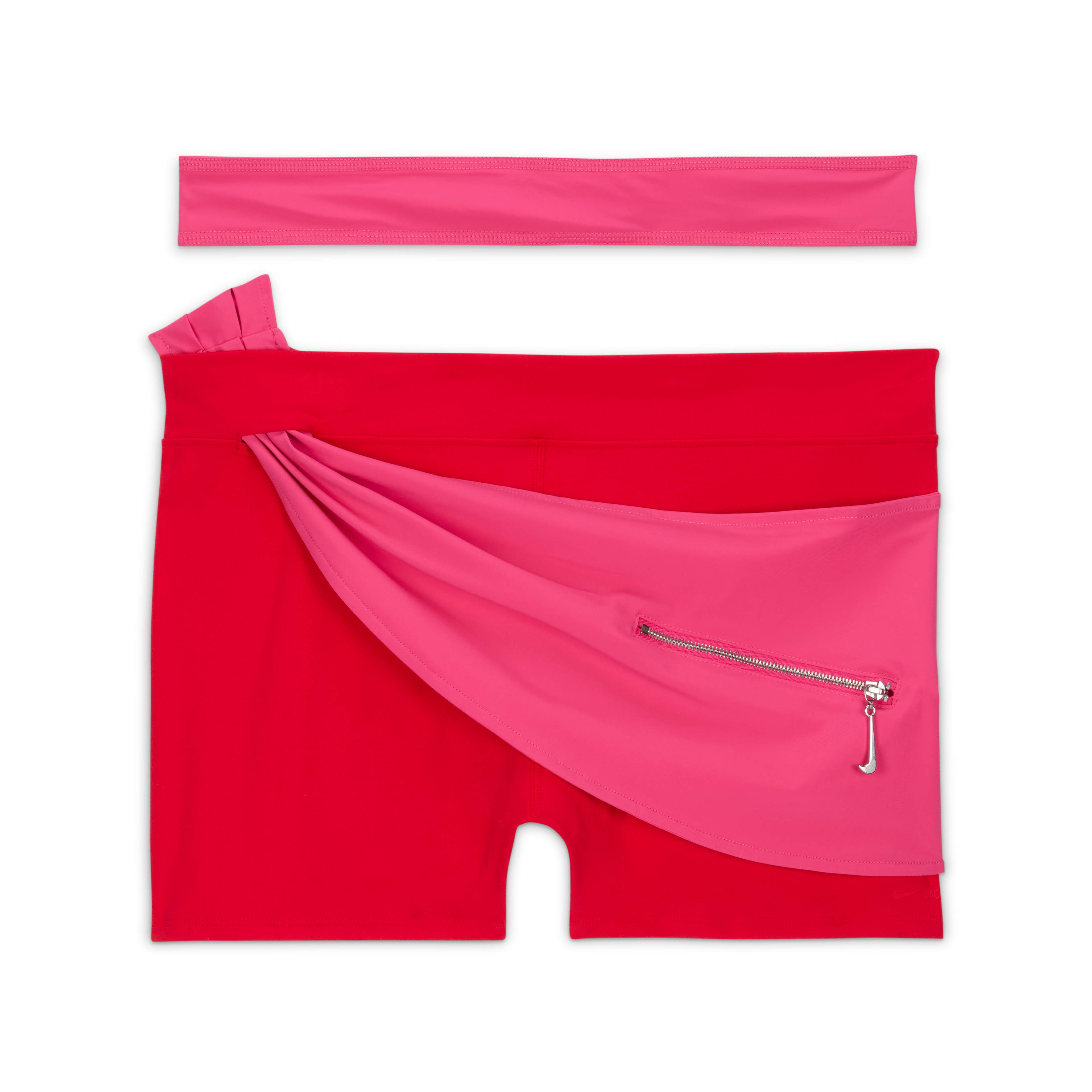 Overhead view of the Nike x Jacquemus Women's Layered Short in university red and watermelon pink. The red short stretch shorts include pink wraparound material at the waist, which holds a small pocket with silver metal hardware and a zipper pull in the shape of a Swoosh. You see the red wraparound strap positioned above the shorts, which float on a black background.