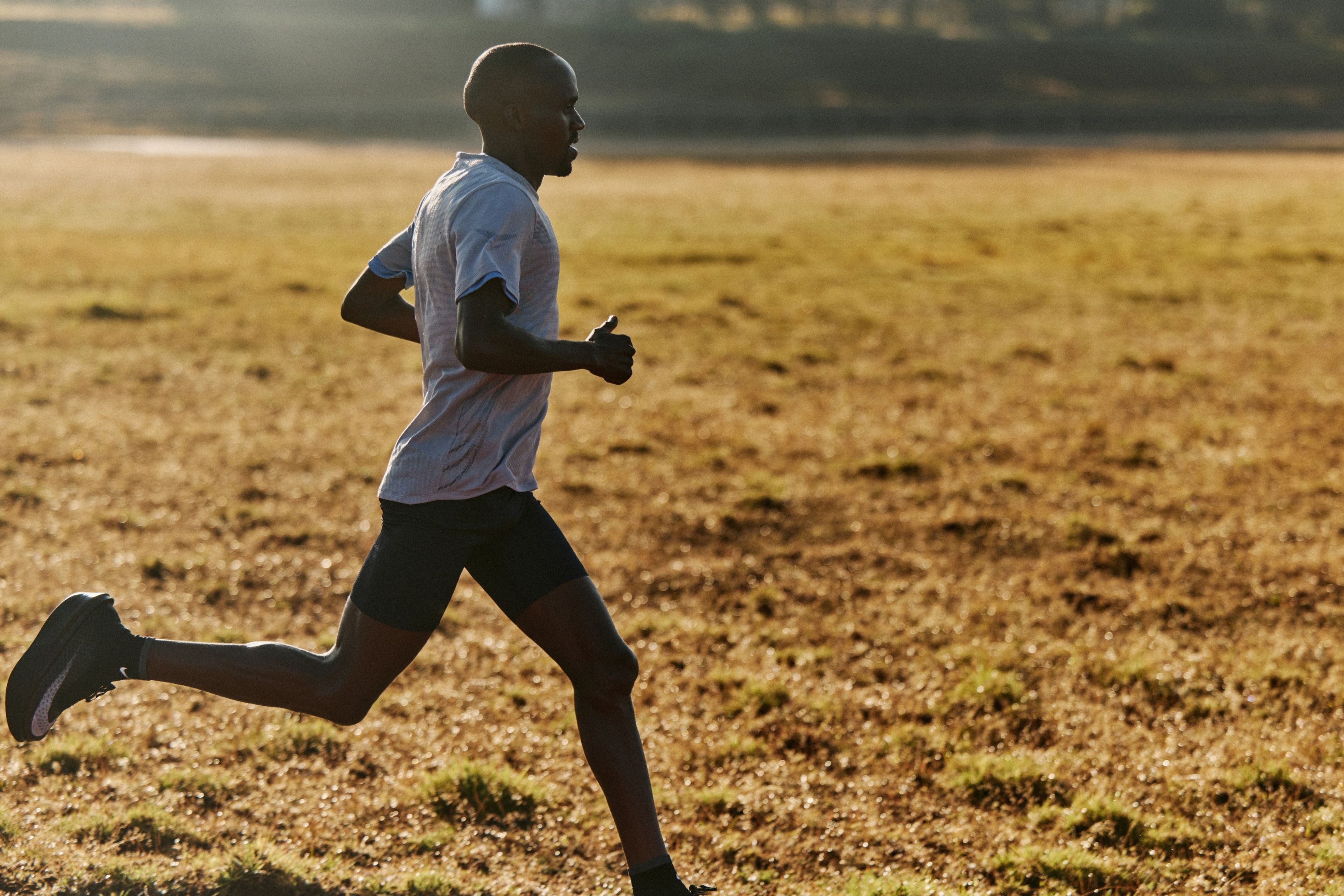 Nike athlete Jacob Kiplimo strides across an open grassland wearing Apex running shoes.
