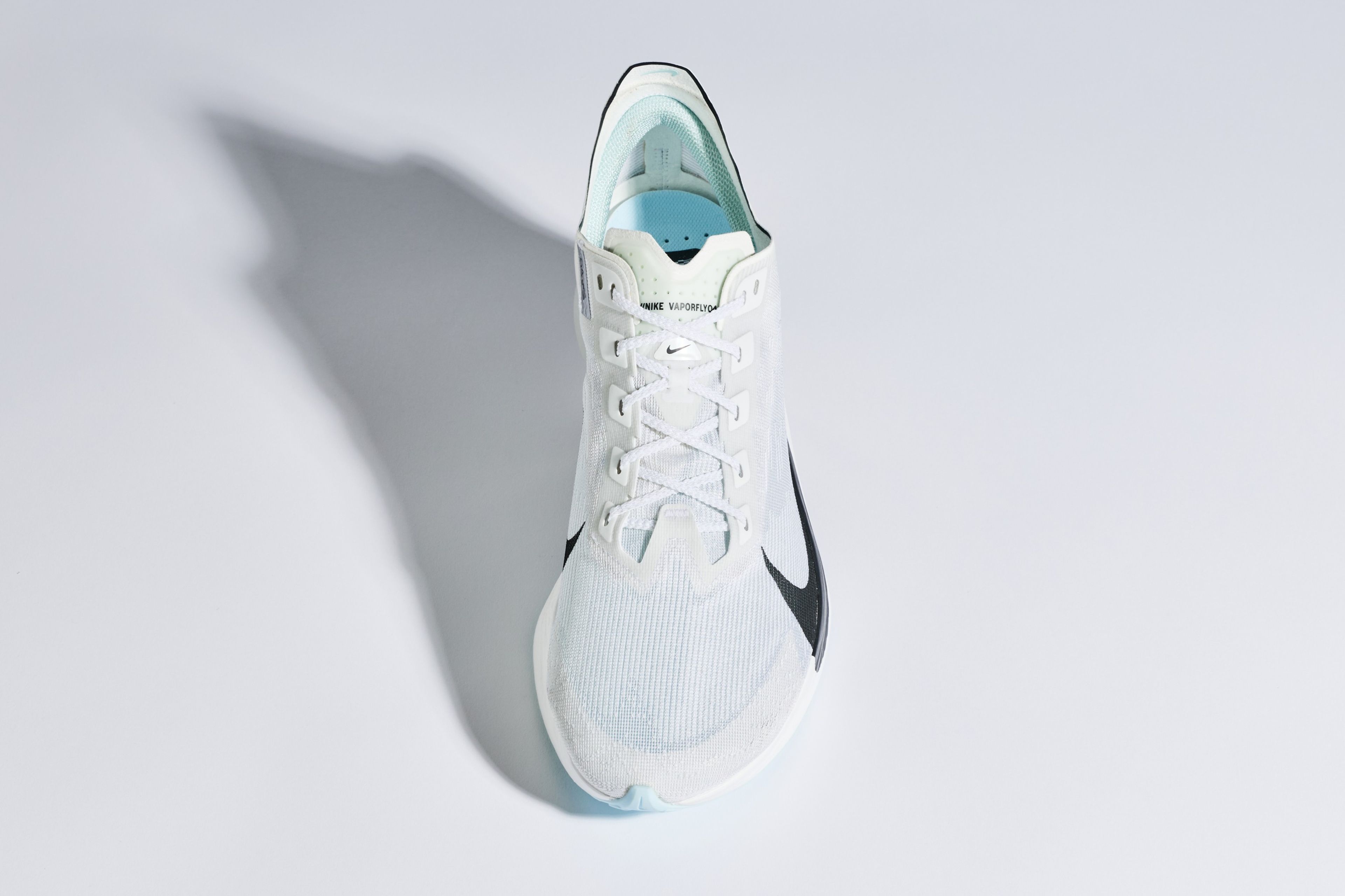 Nike Vaporfly 4 running shoe with black Swoosh, white laces, and light blue insole, shot from above on a gray background.