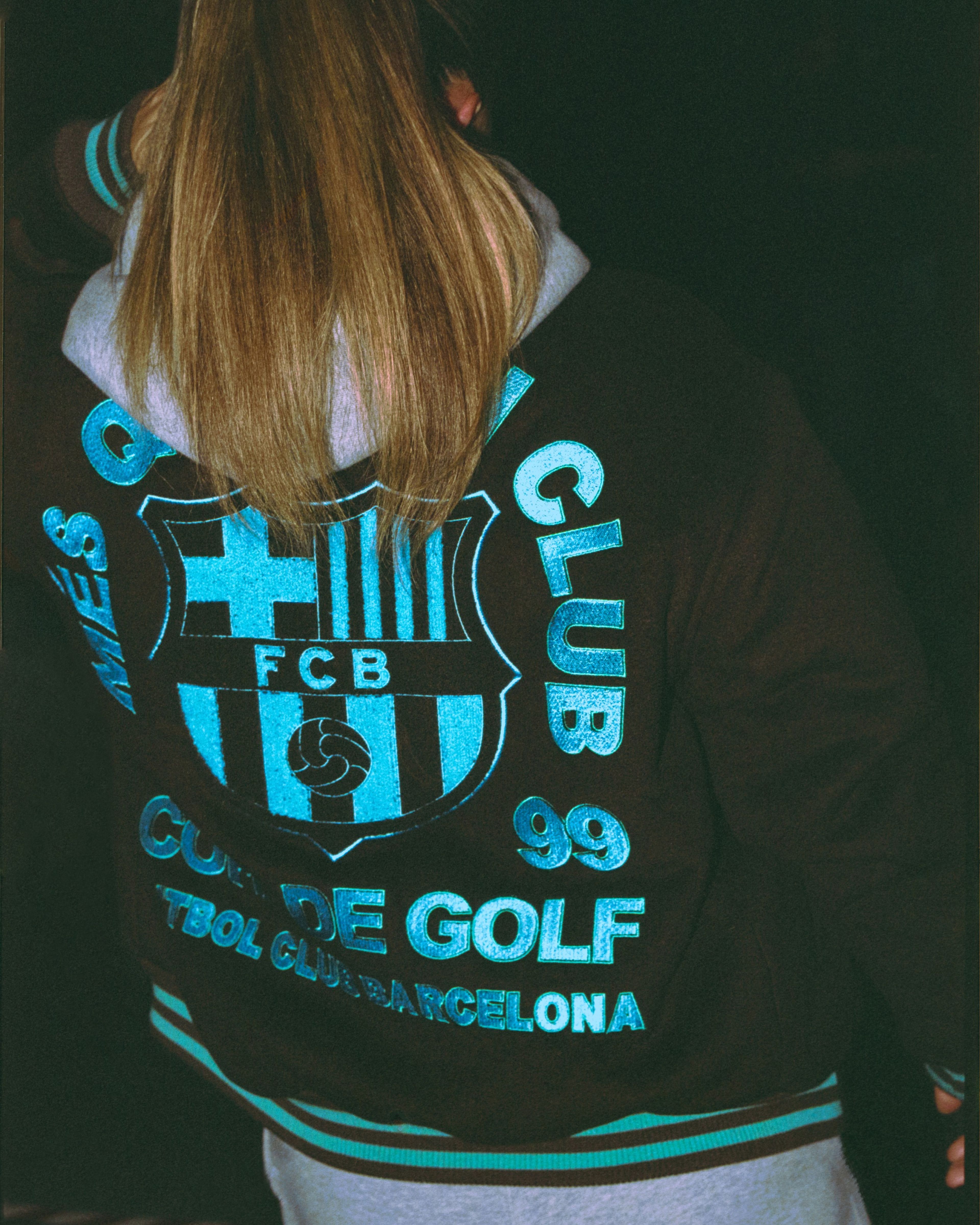 Back view of a person wearing a brown Nike x FC Barcelona x GOLF WANG (GOLF) varsity jacket.