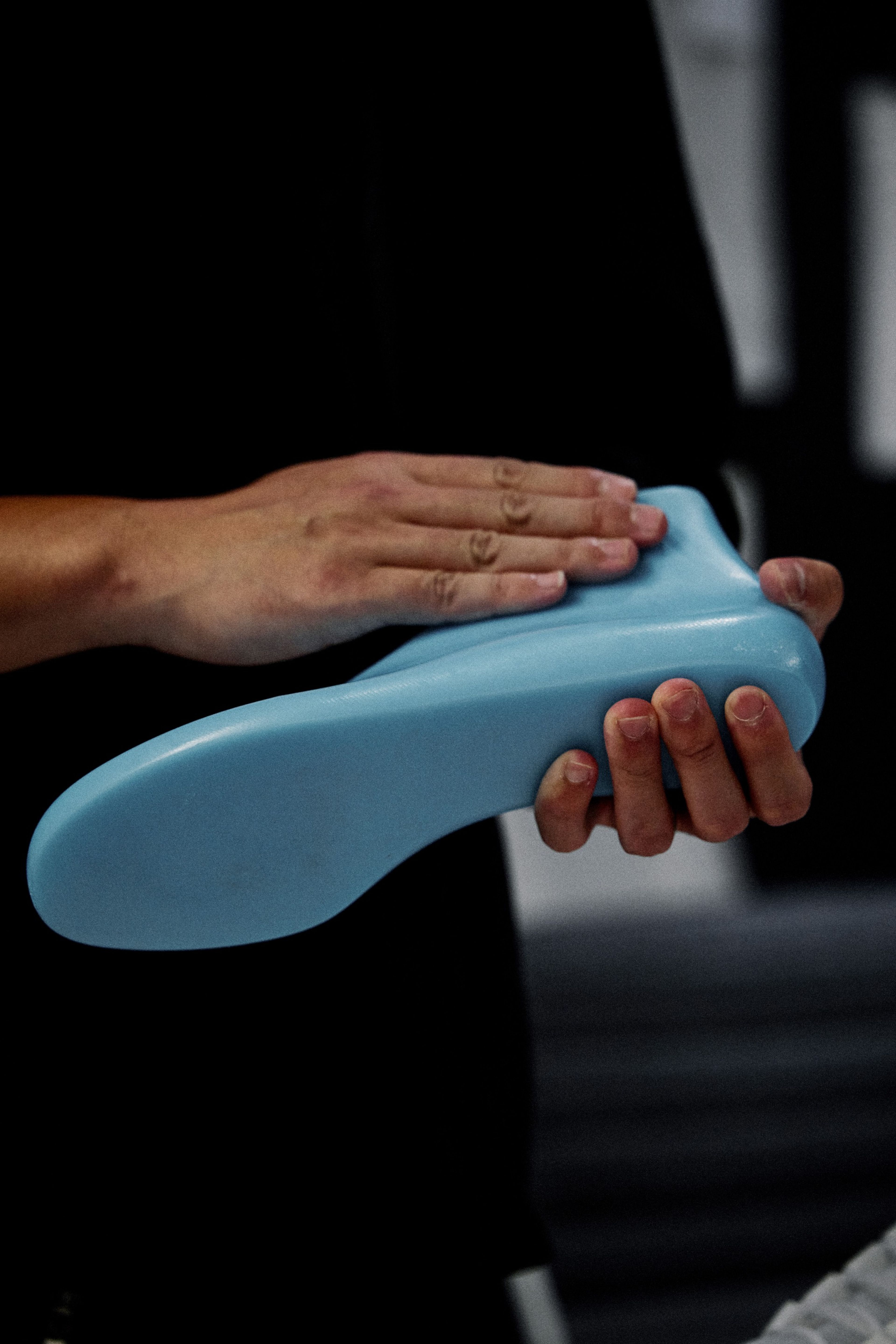 A blue last in the shape of a foot and ankle is held in two hands