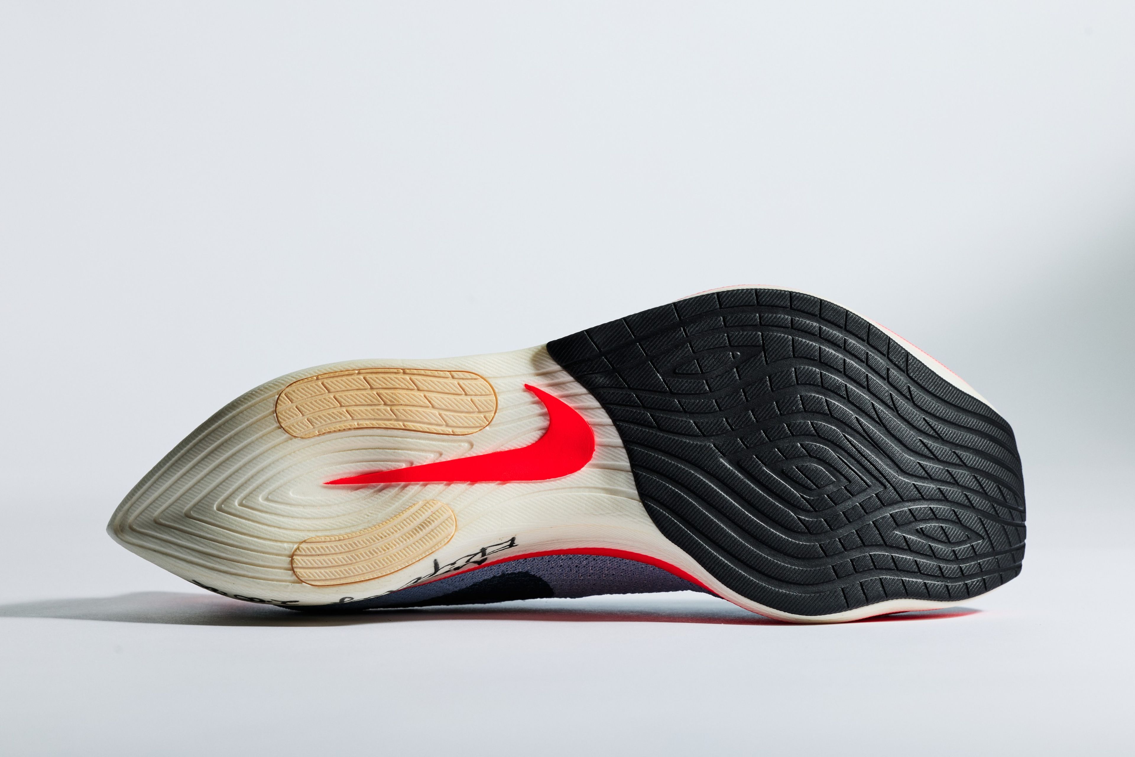 Bottom view of Nike ZoomX Vaporfly Elite outsole showing red Swoosh logo, black rubber tread pattern, and cream foam midsole on a light gray background.