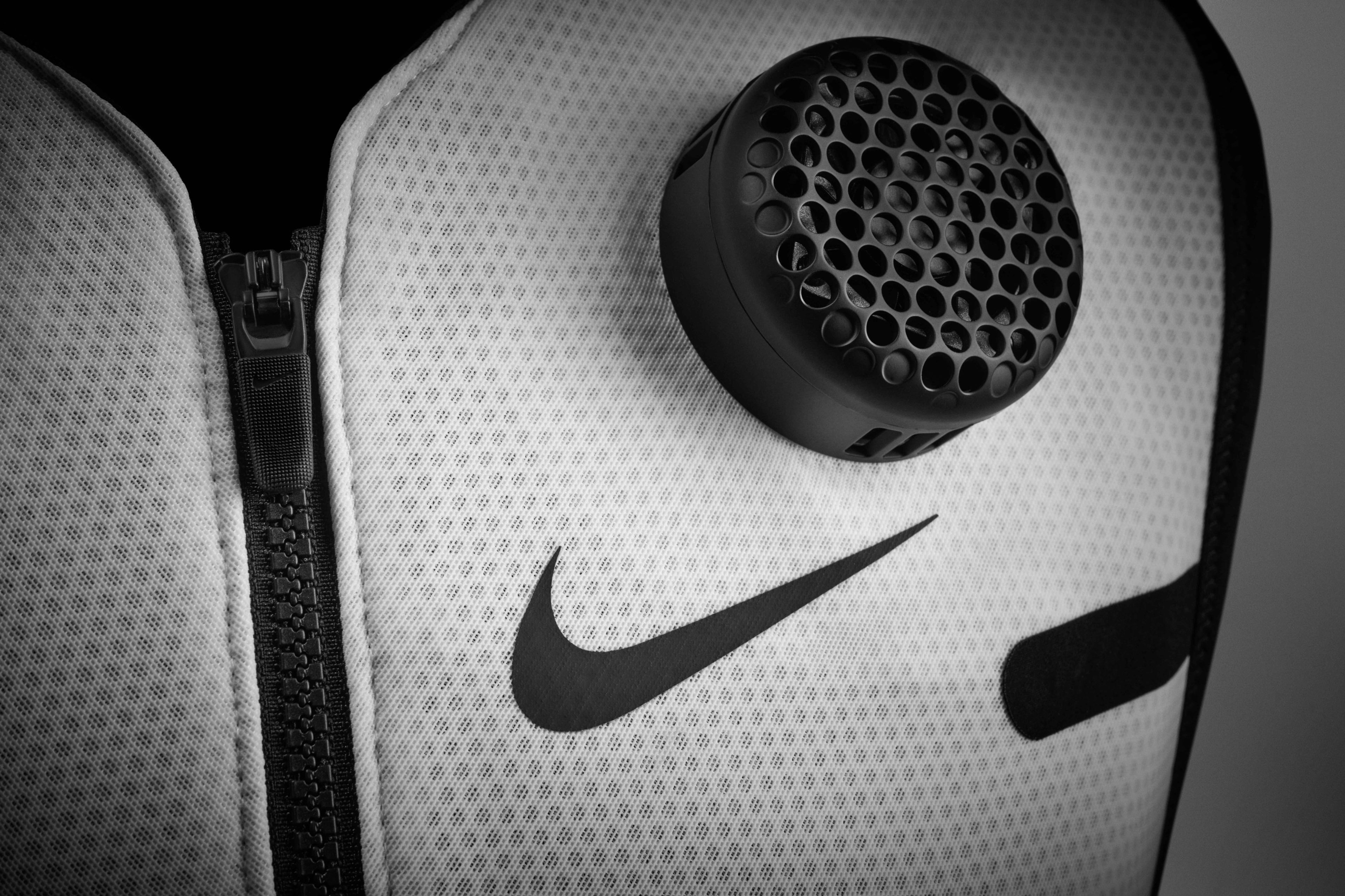 Detail view of a thermal module sitting on the front of a Nike x Hyperice vest, above a black Nike Swoosh. The white vest sits against a grey background.