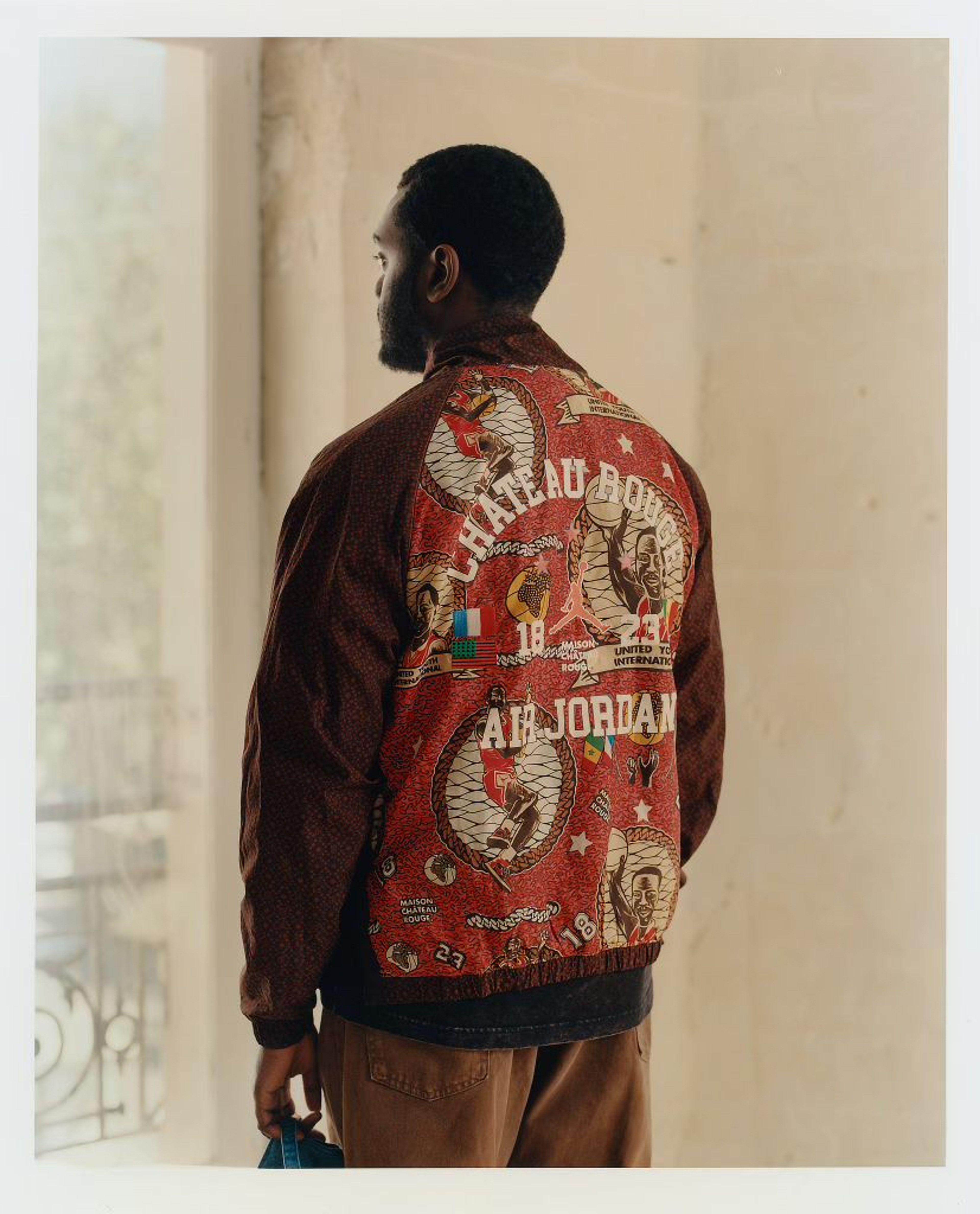 Back angle view of Youssouf Fofana wearing a Chateau Rouge Air Jordan jacket and looking out a window.