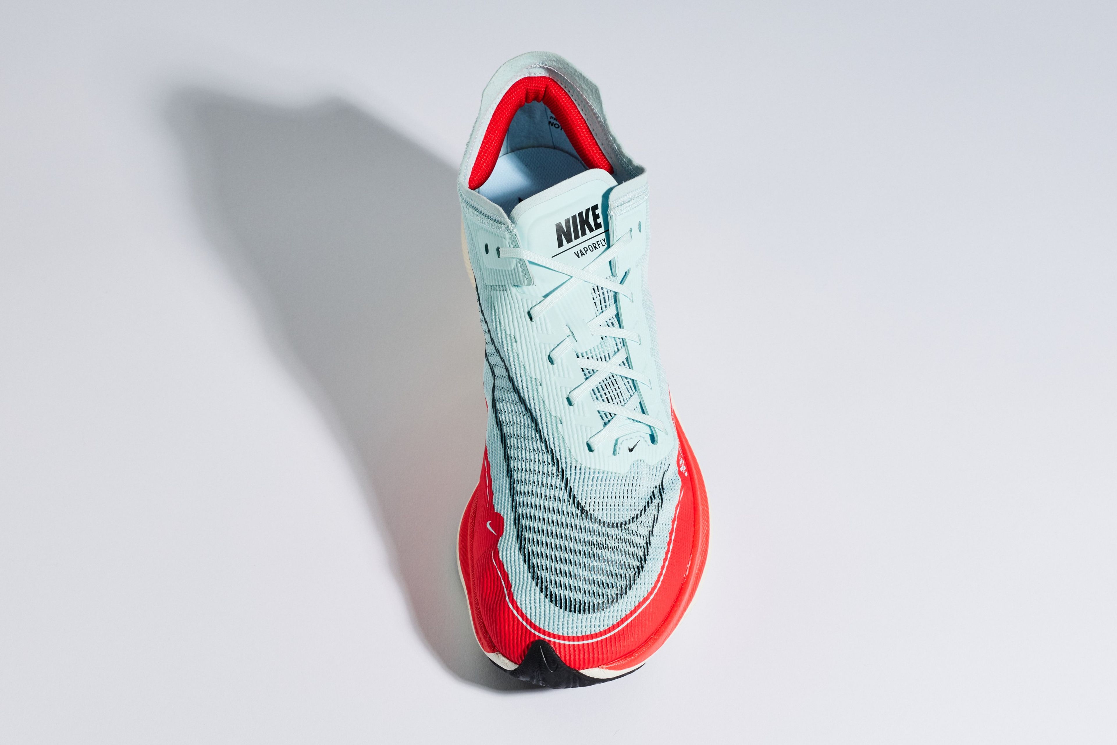 Nike Vaporfly NEXT% 2 running shoe with light blue knit upper, Nike Swoosh, and red midsole, shot from above on a white background.
