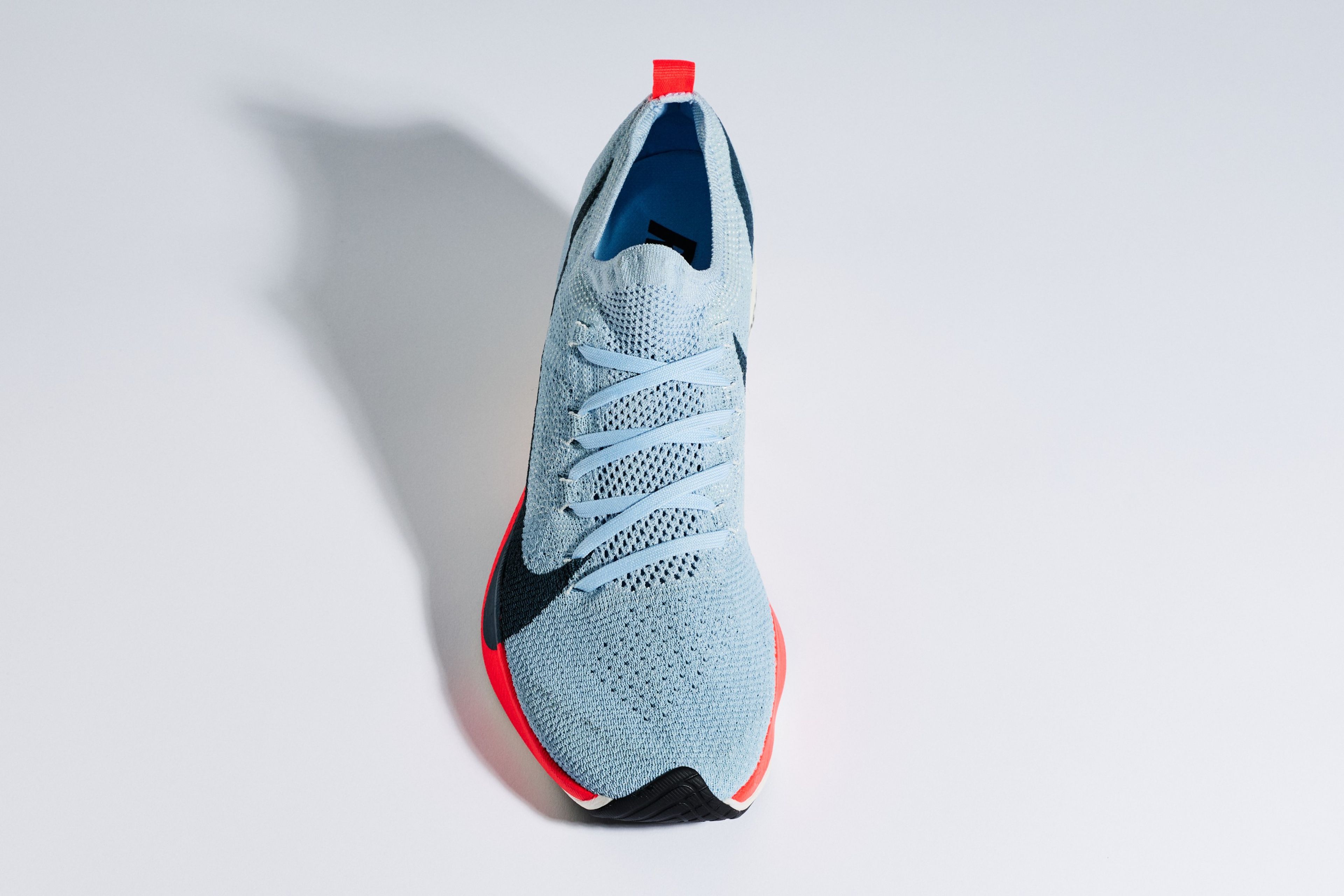 Top-down studio shot of a Nike Vaporfly Elite running shoe in light blue with a red midsole, black Swoosh, and red pull tab on white background.
