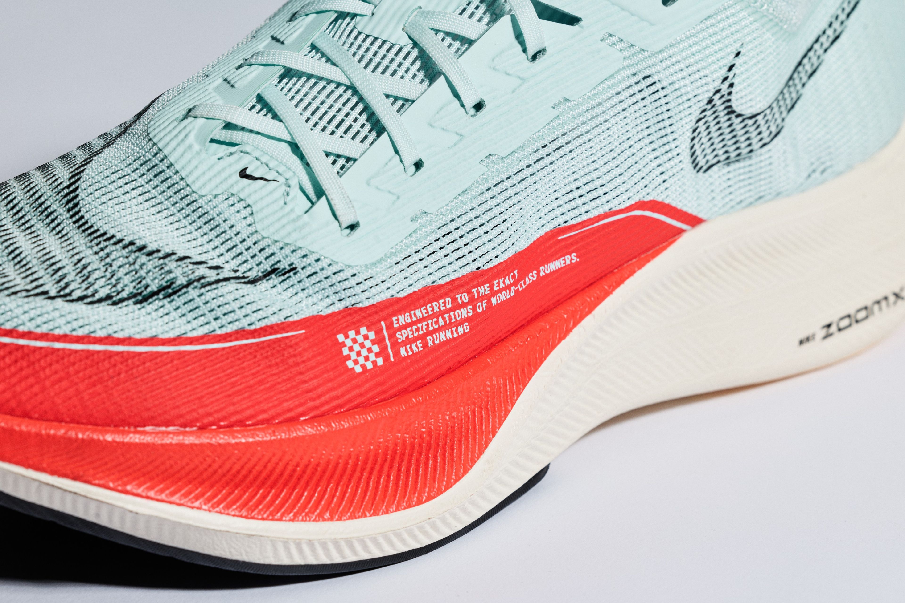 Close-up of a Nike ZoomX Vaporfly Next% 2 running shoe in light blue with a bright red midsole, showing the lacing system and printed text detail.