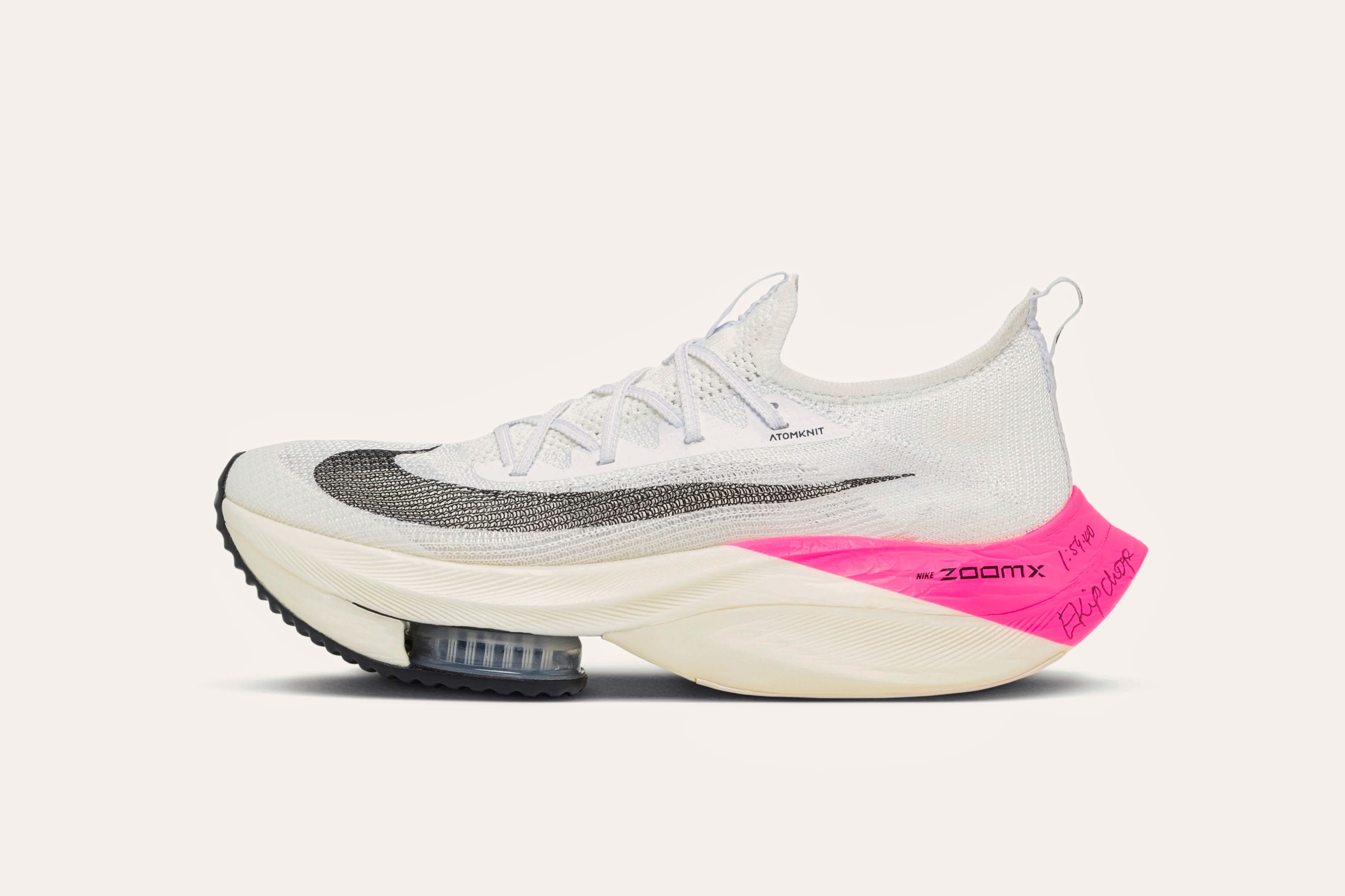 A white sneaker with a grey swoosh on the front and a pink heel in the back that has "ZOOMX" printed on it and Eliud Kipchoge's signature written on it in pen.