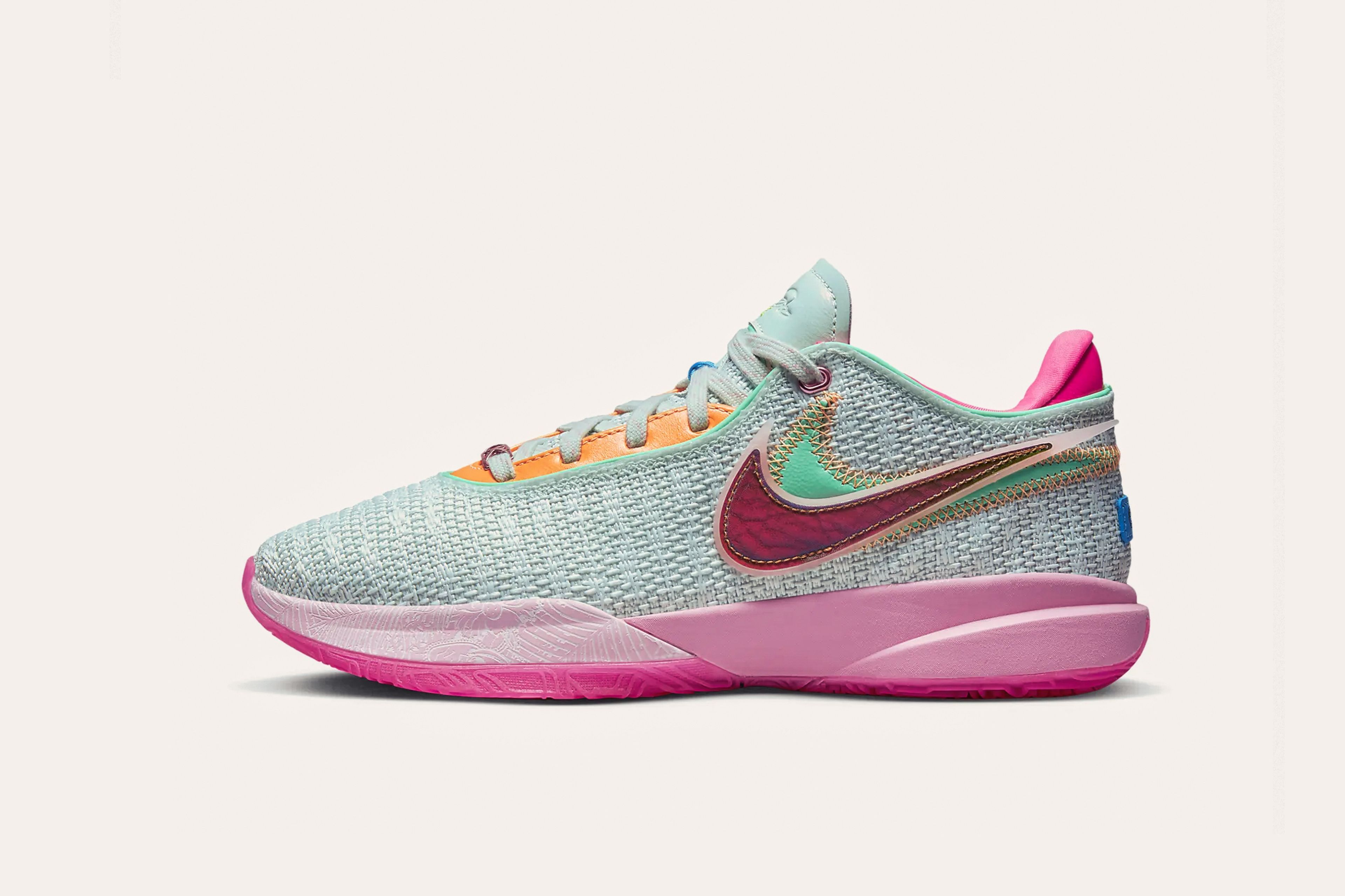A light teal sneaker with a maroon Nike swoosh layered on top of a teal swoosh on the side, orange shoelace tabs, a pink sole, and a pink rear cuff.