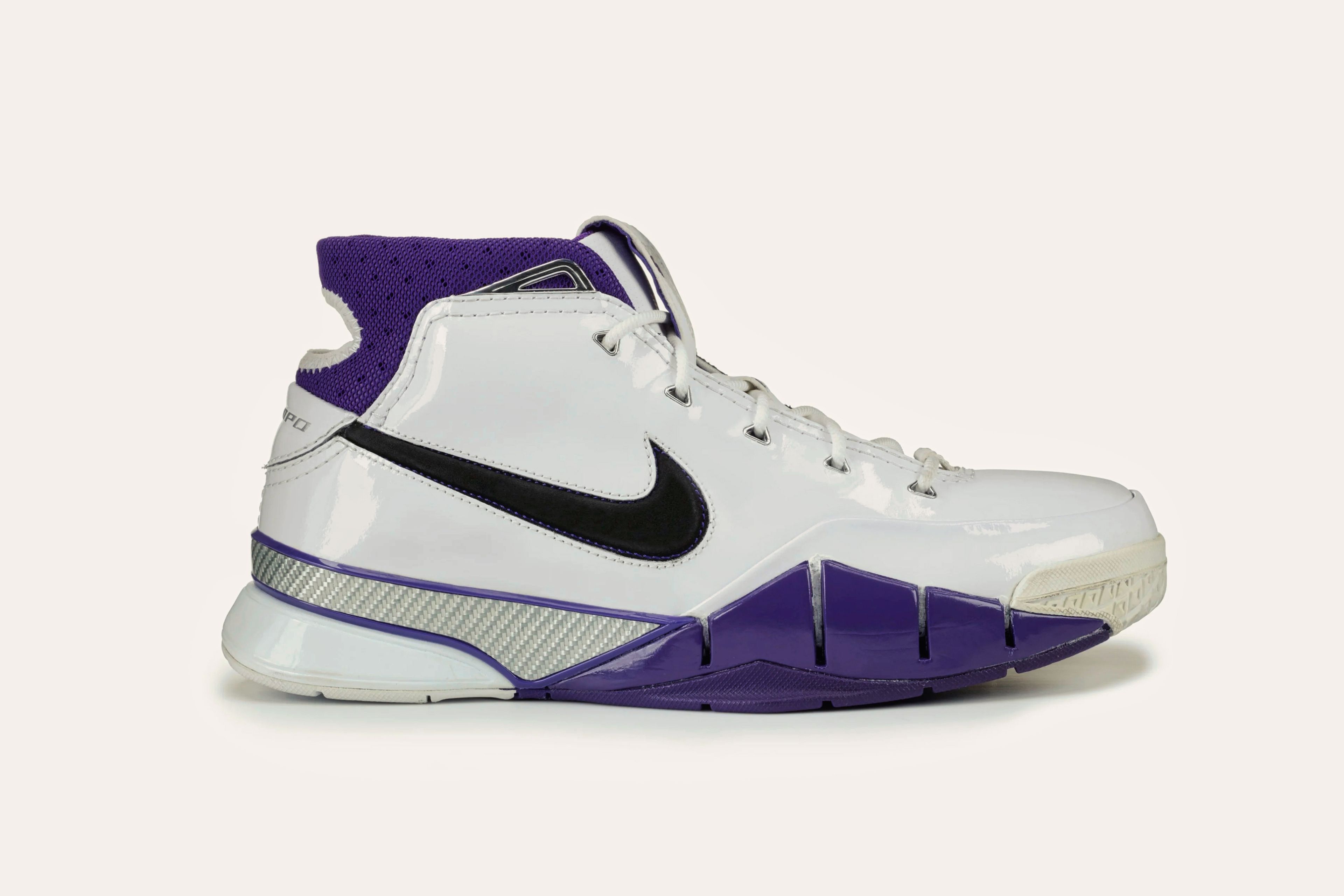 A white sneaker with a black swoosh on the side of the angle, an indigo sole on the toe region, and an indigo cuff.