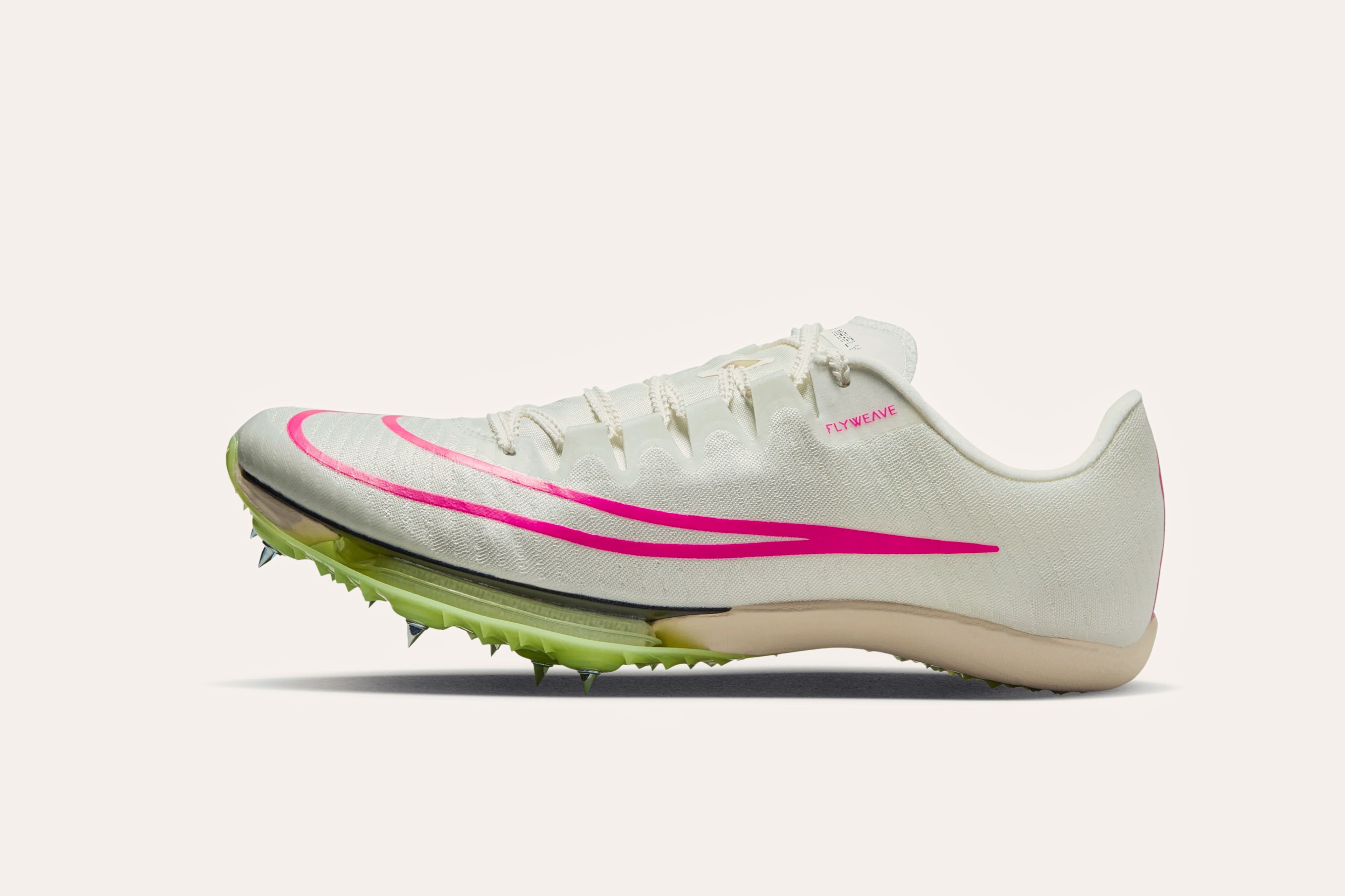 A white sneaker with "Flyweave" printed by the front of the cuff, a pink outline of a Nike swoosh, and a light green sole with spiked cleats.