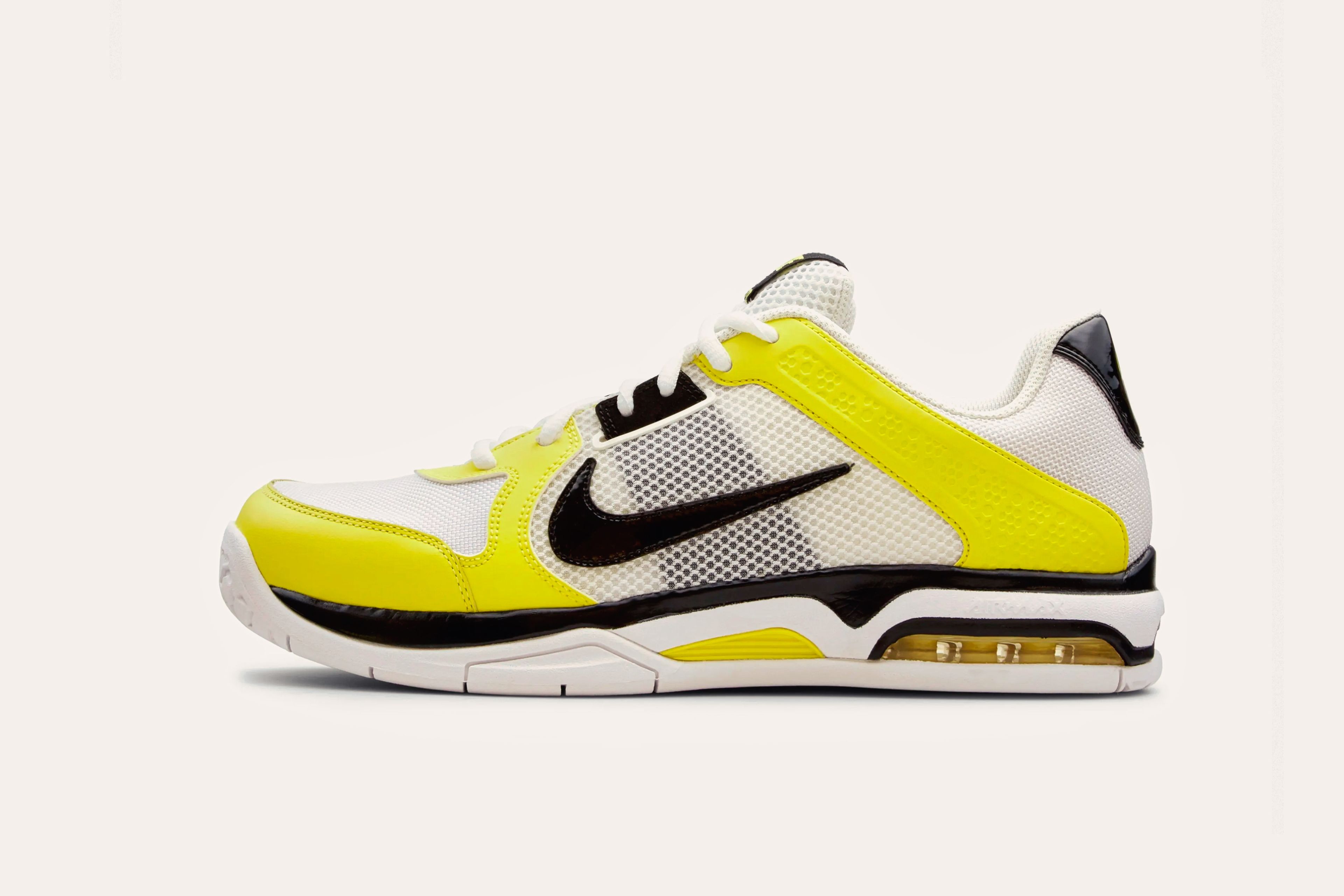A white sneaker with a black Nike swoosh on the side mesh, a bright yellow stripe across the toe and heel, and a bright yellow toecap.
