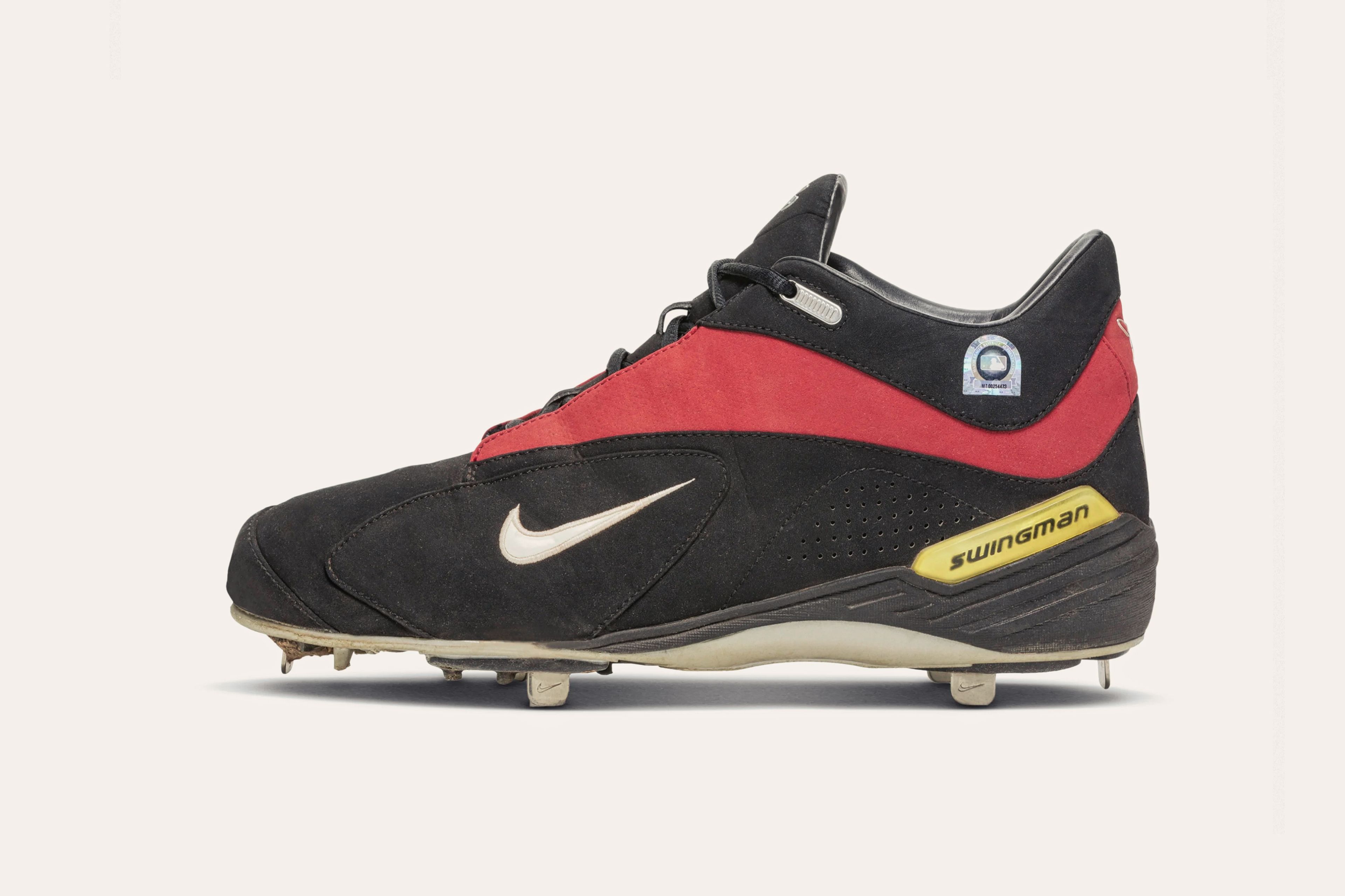 A dark grey sneaker with a small white Nike swoosh on the side, a red stripe around the ankle, a yellow tab on the heel that says "Swingman," and a white sole with cleats.