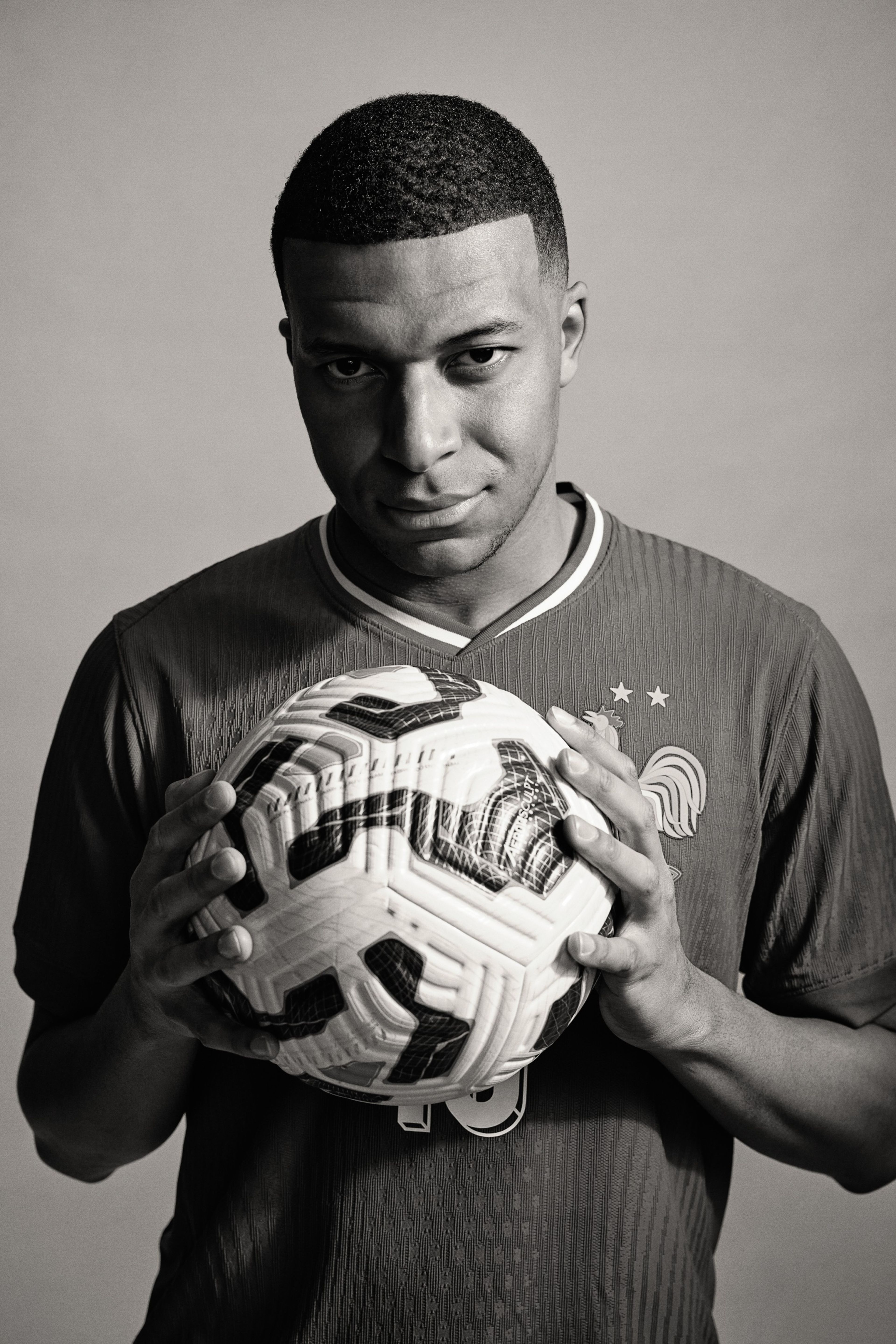 Black and white photo of Kylian Mbappé holding a soccer ball.