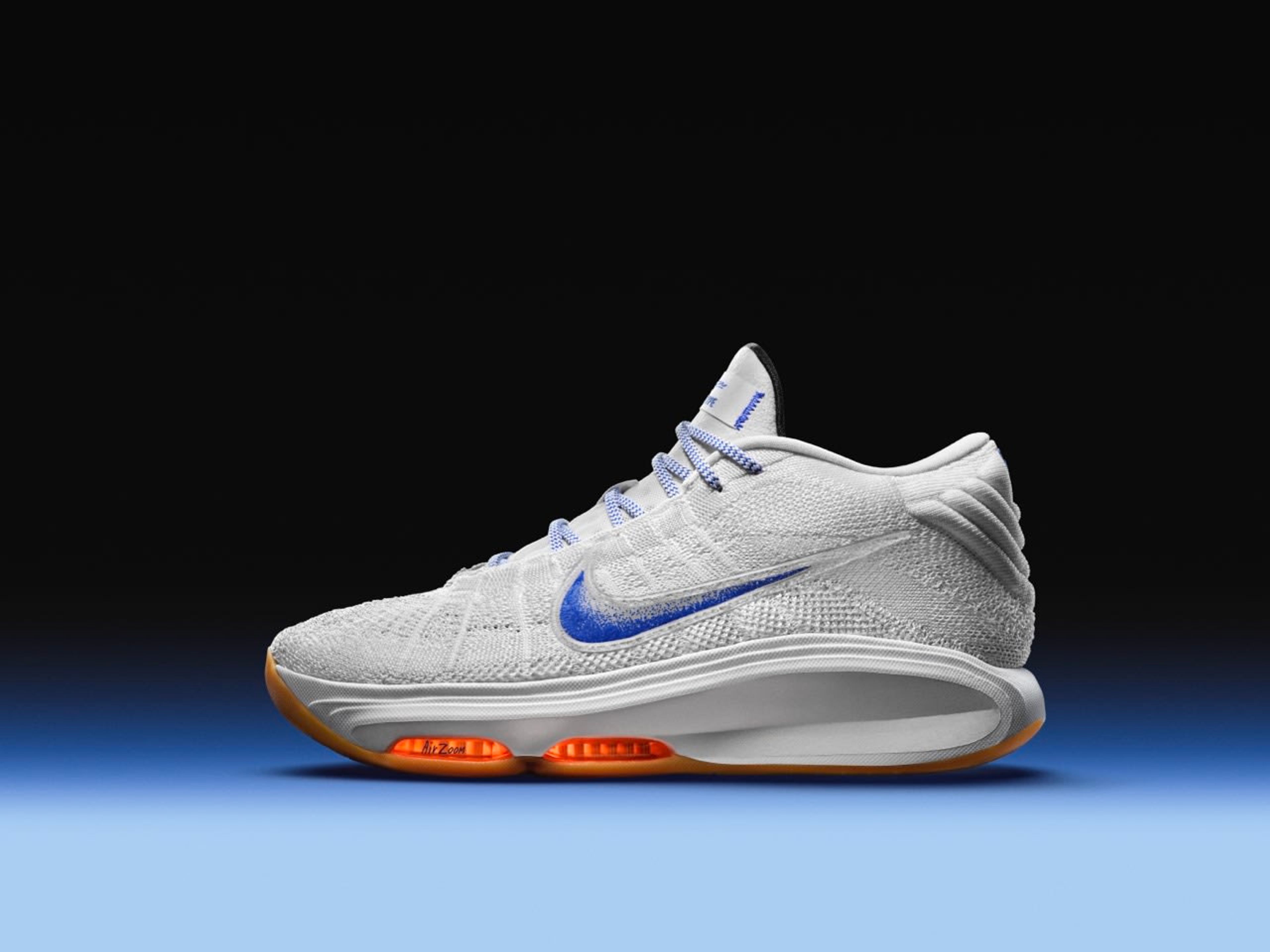 Left view of a Nike GT Hustle 3 basketball shoe in the Blueprint colorway. White upper with a speckled blue Swoosh, orange Air Zoom units, and a gum sole tread. The shoe sits on a blue floor against a black background.
