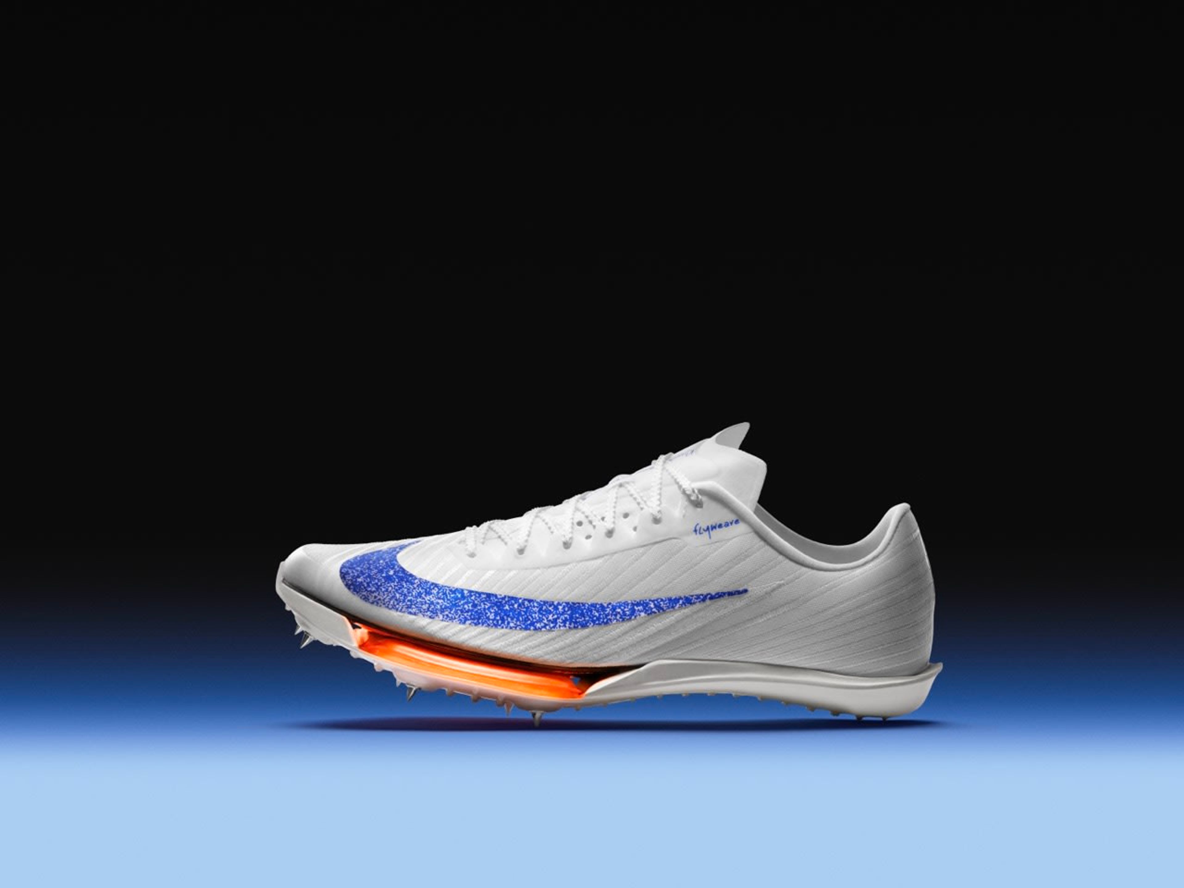 Left side view of Nike Maxfly 2 spikes in Blueprint colorway. White upper with a speckled blue swoosh, orange Air Zoom unit, and a white spike plate. The shoe sits on a blue floor with a black background.
