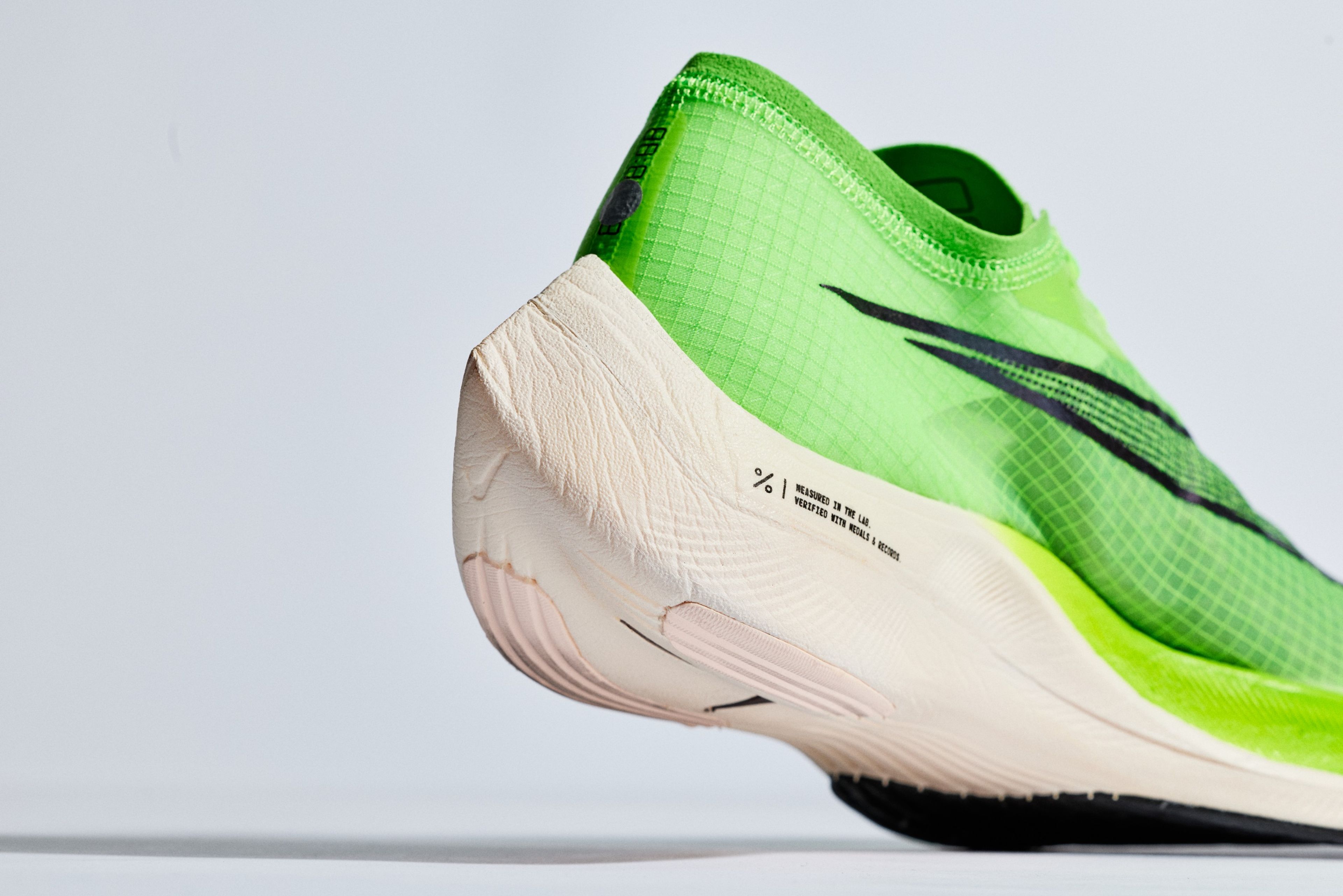 Close-up of a bright green Nike ZoomX Vaporfly Next% running shoe showing the ZoomX white midsole with performance text detailing.