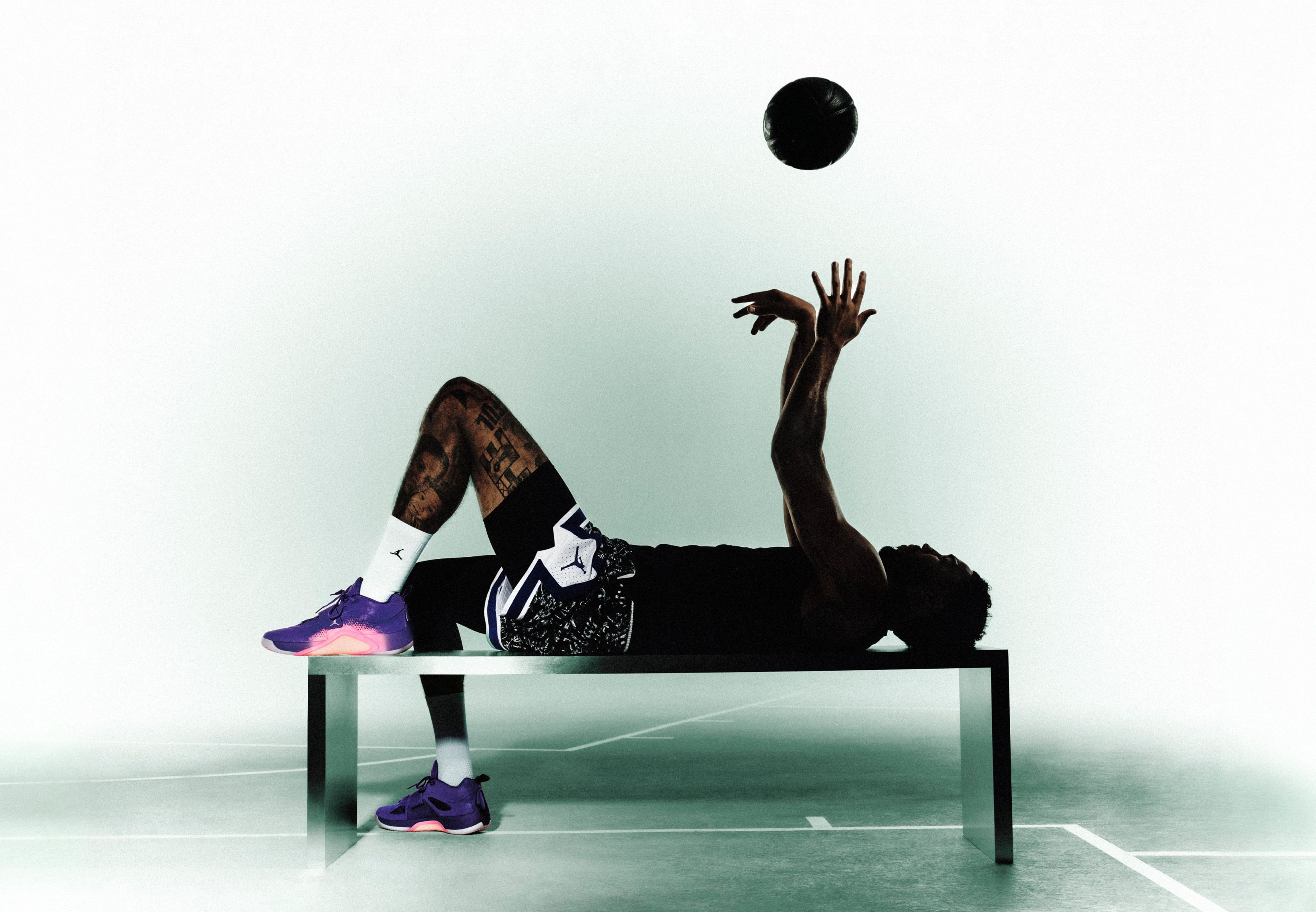 Jordan Brand athlete Jayson Tatum lays on a table, tossing a basketball into the air while wearing his new Tatum 5 signature shoe.