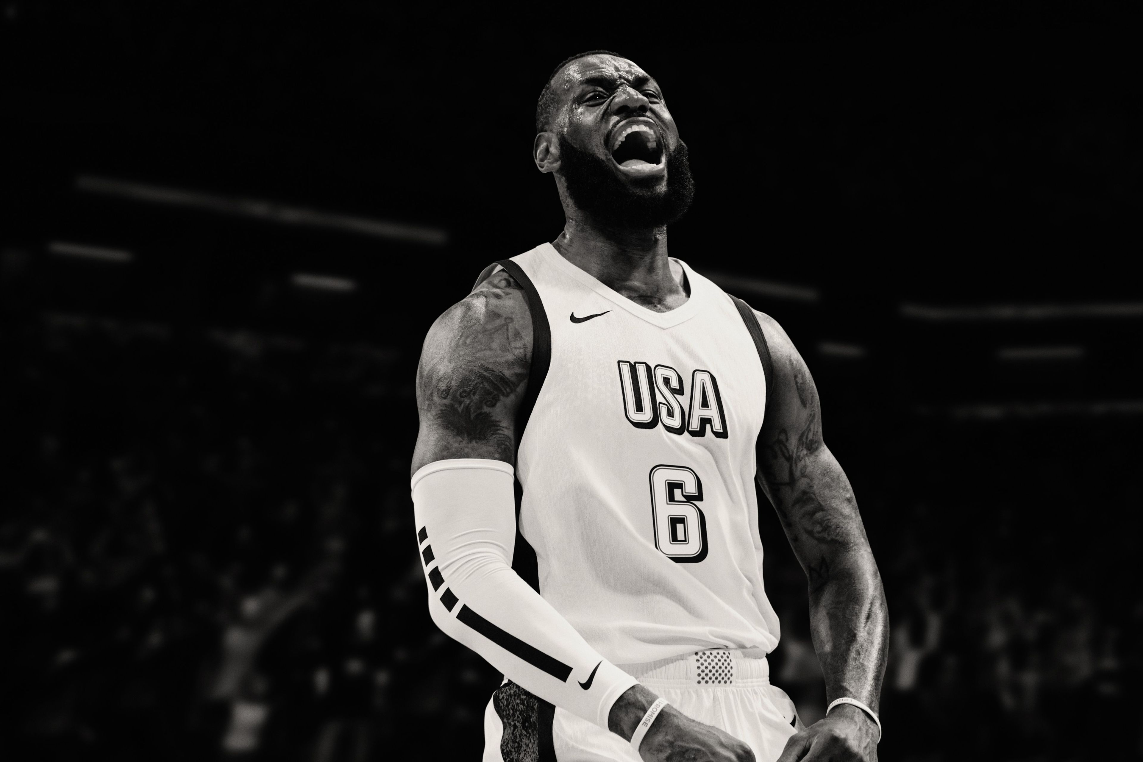 Black and white image of Nike Athlete, Lebron James, wearing Team USA Basketball jersey and a white Nike Pro Elite sleeve. He yells enthusiastically.