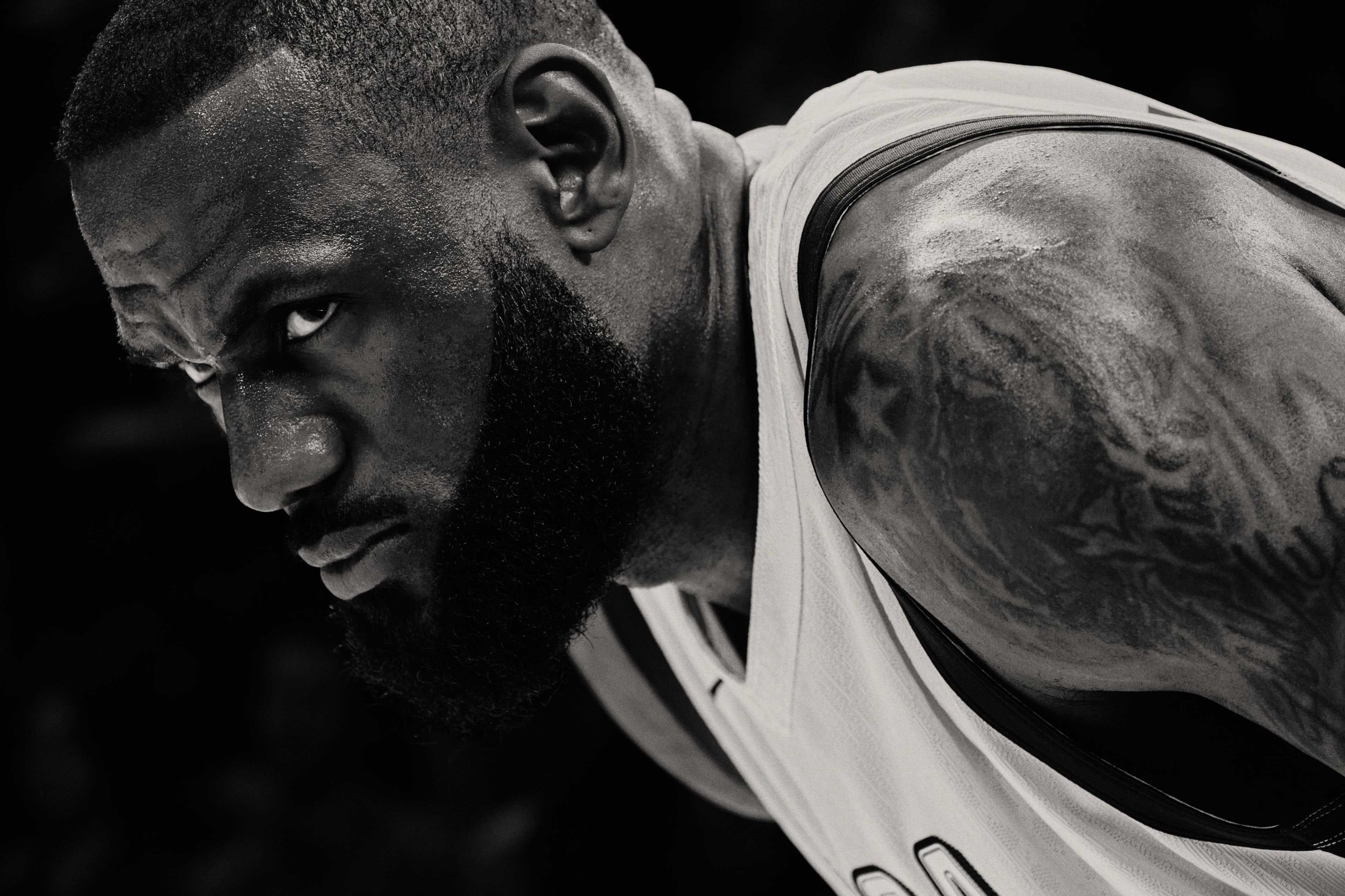 Black and white close up of Lebron James in a white Team USA jersey. Lebron is bent over with is eyes looking over to a competitor, ready for action.