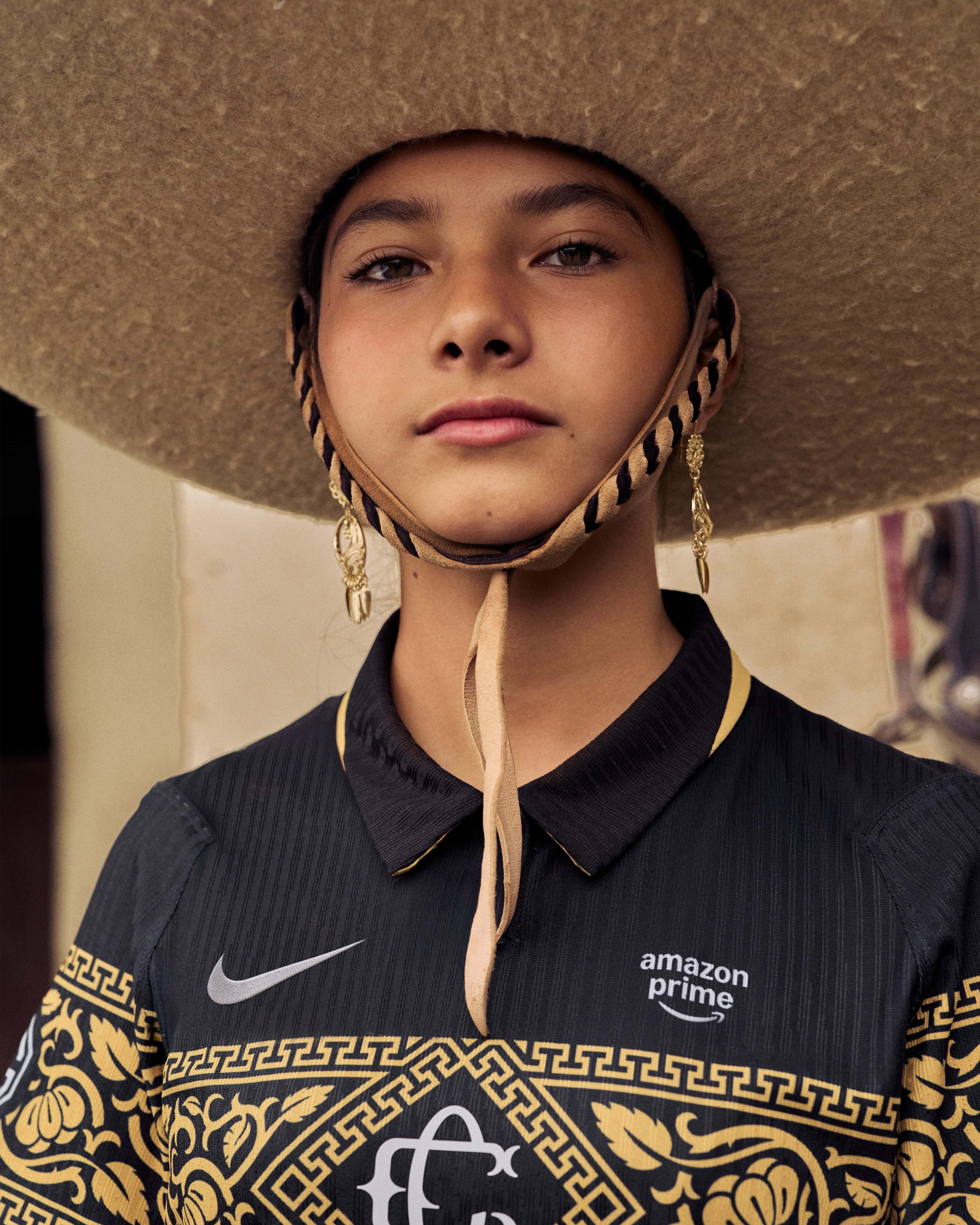 A young person wearing a Mexican sombrero and an ornate black and gold Chivas de Guadalajara soccer jersey.