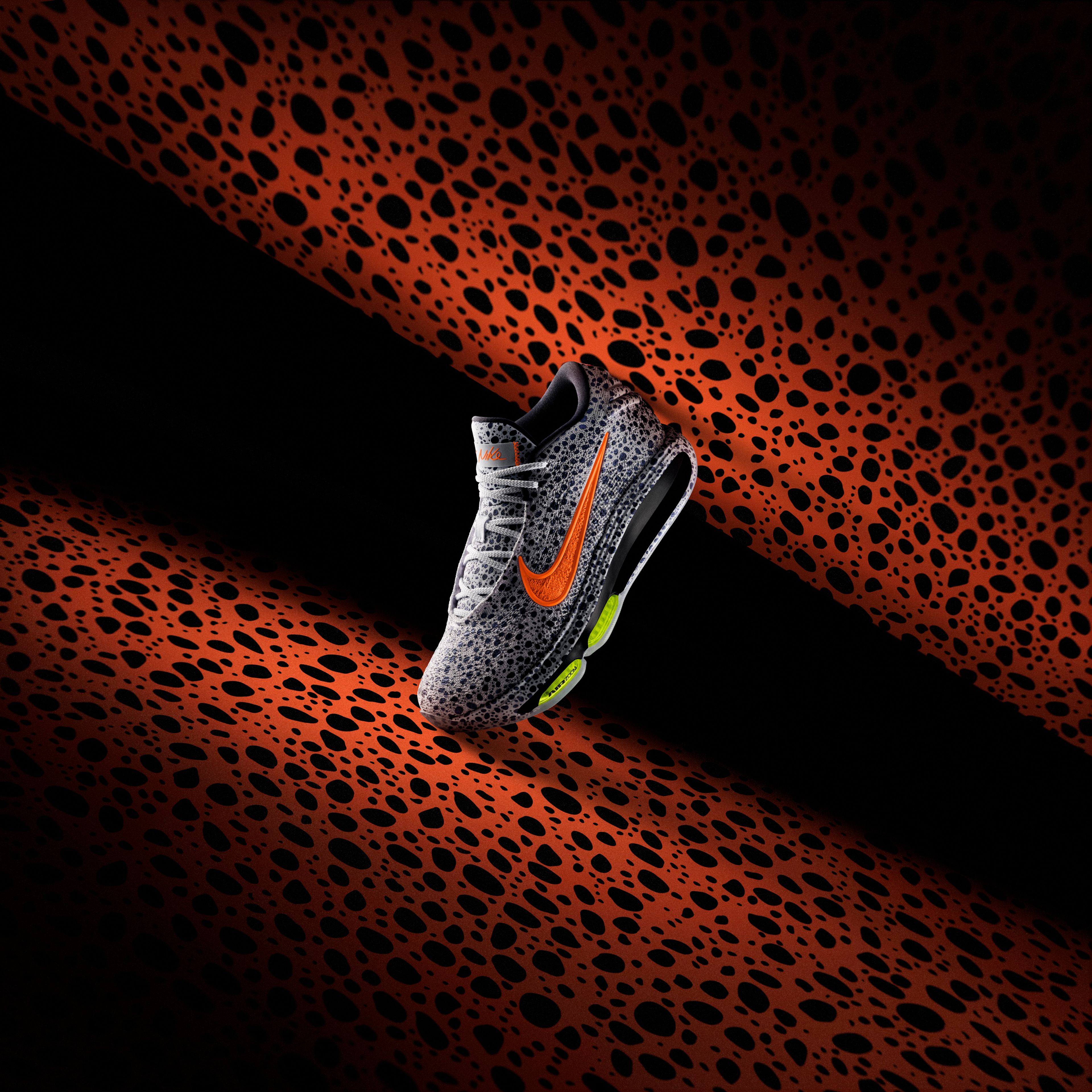 Left view of a Nike GT Hustle 3 basketball shoe in the Electric colorway, which is a gray upper with a speckled blue/black pattern, orange Swoosh, and Volt Air Zoom units. The shoe sits on an orange Electric pattern background.