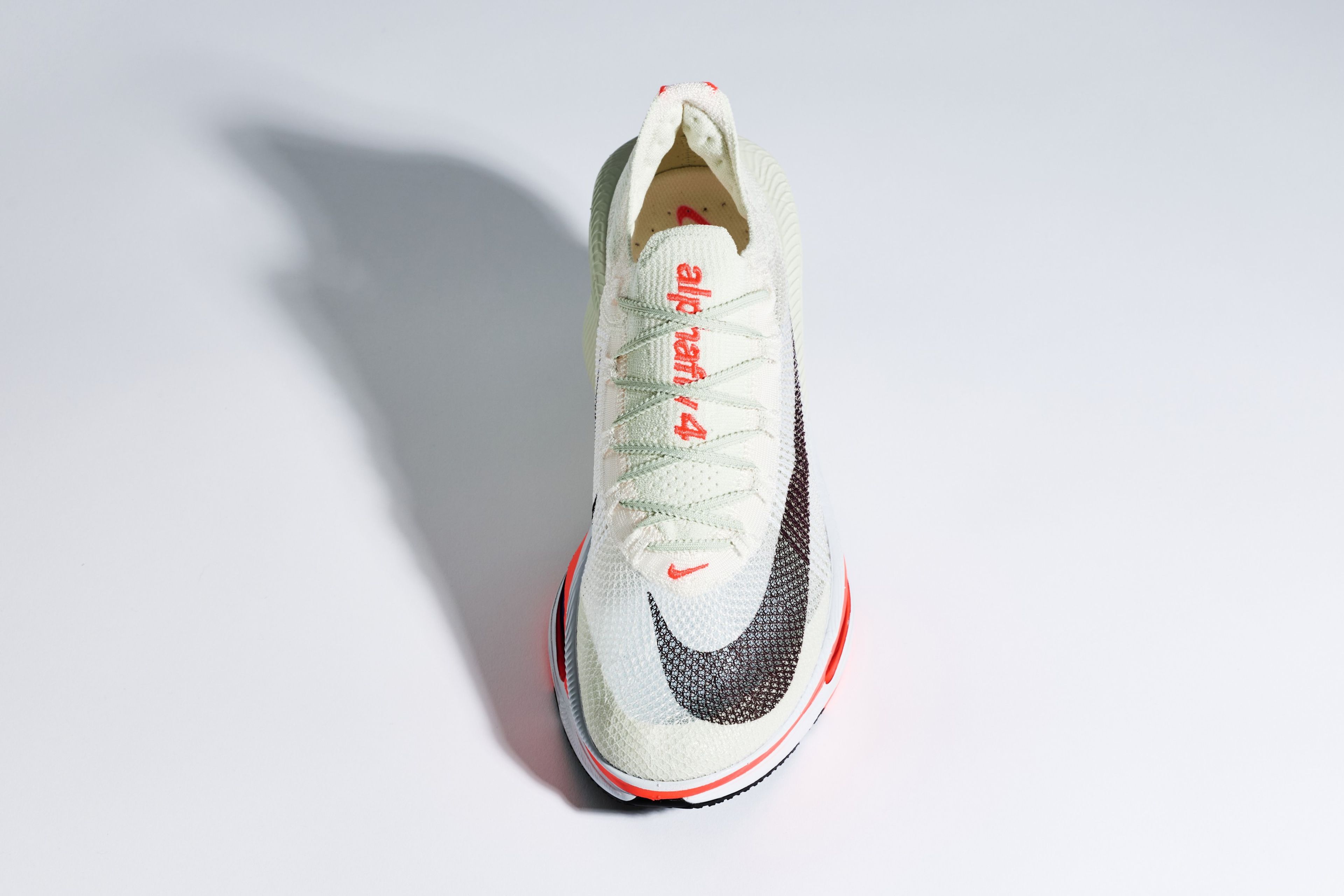 Top-down studio view of Nike Alphafly 4 marathon racing shoe in white with mint green laces, red accents, Nike Swoosh.