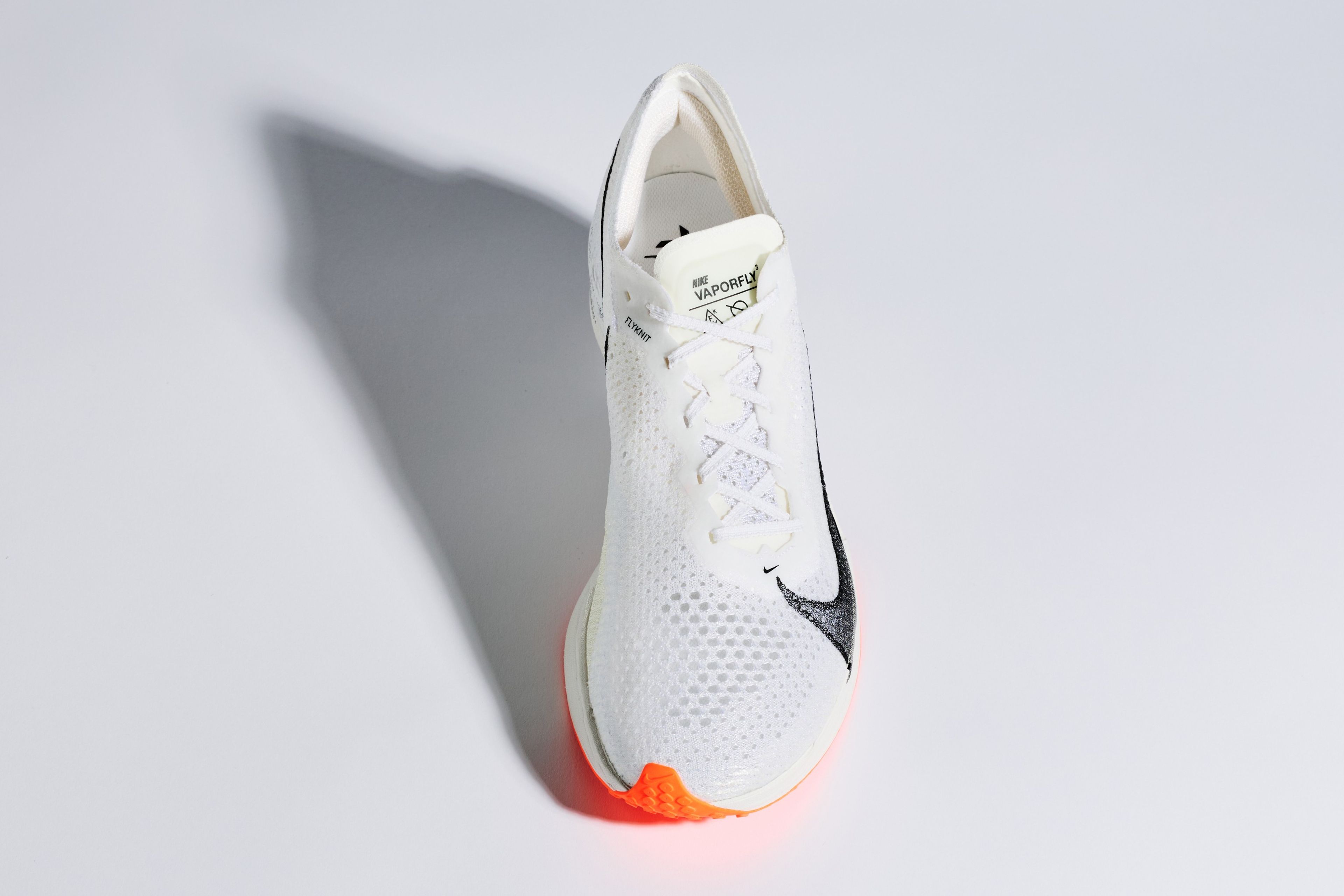 Nike Vaporfly 3 running shoe in white with black Swoosh and orange sole accents, shown from above against a light grey background.