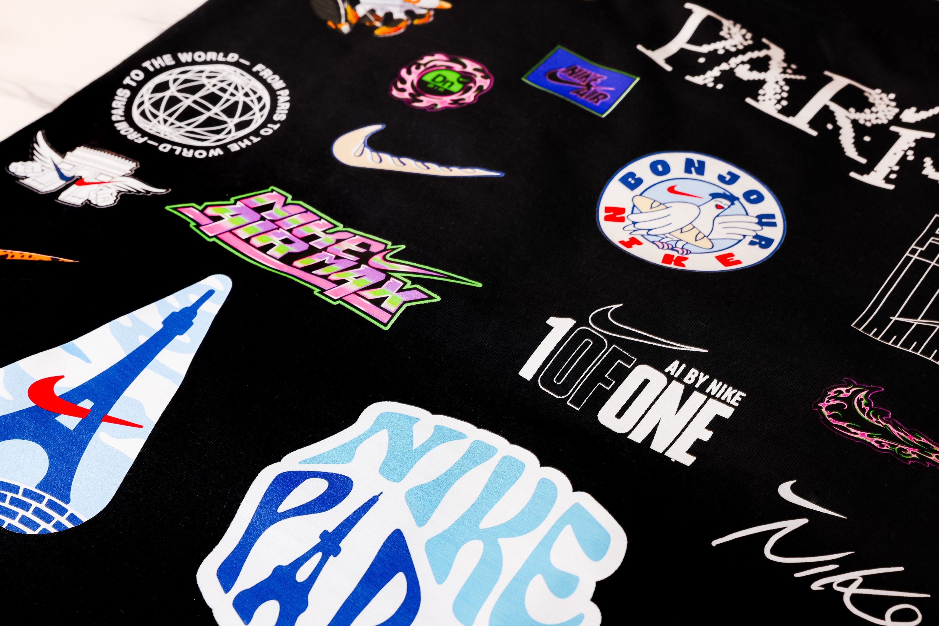 Situated on top of a black background, we see a spectrum of example of the AI-generated designs athletes can create and use to customize Nike apparel. The designs include customized Swooshes, the word PARIS, and Nike logos.