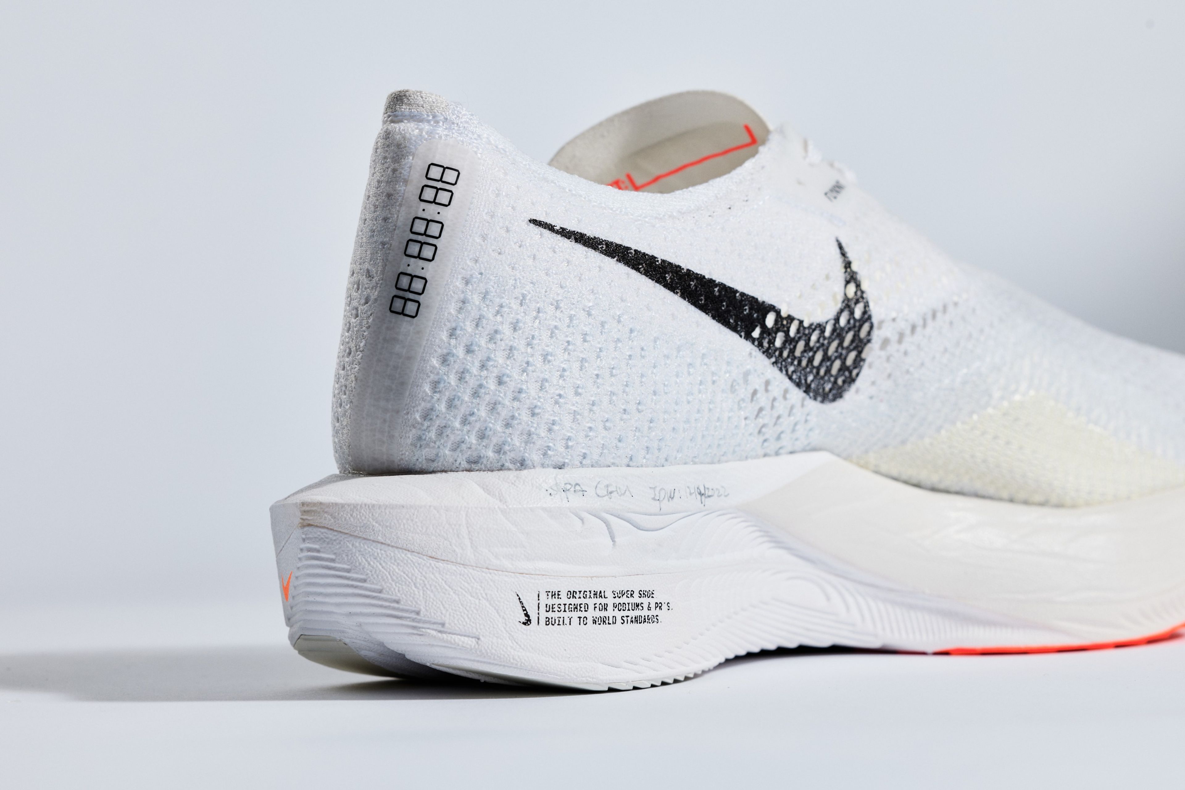 Nike Vaporfly 3 running shoe in white with black Swoosh, orange accents, timer graphic on heel, and The Original Super Shoe text on thick foam midsole.