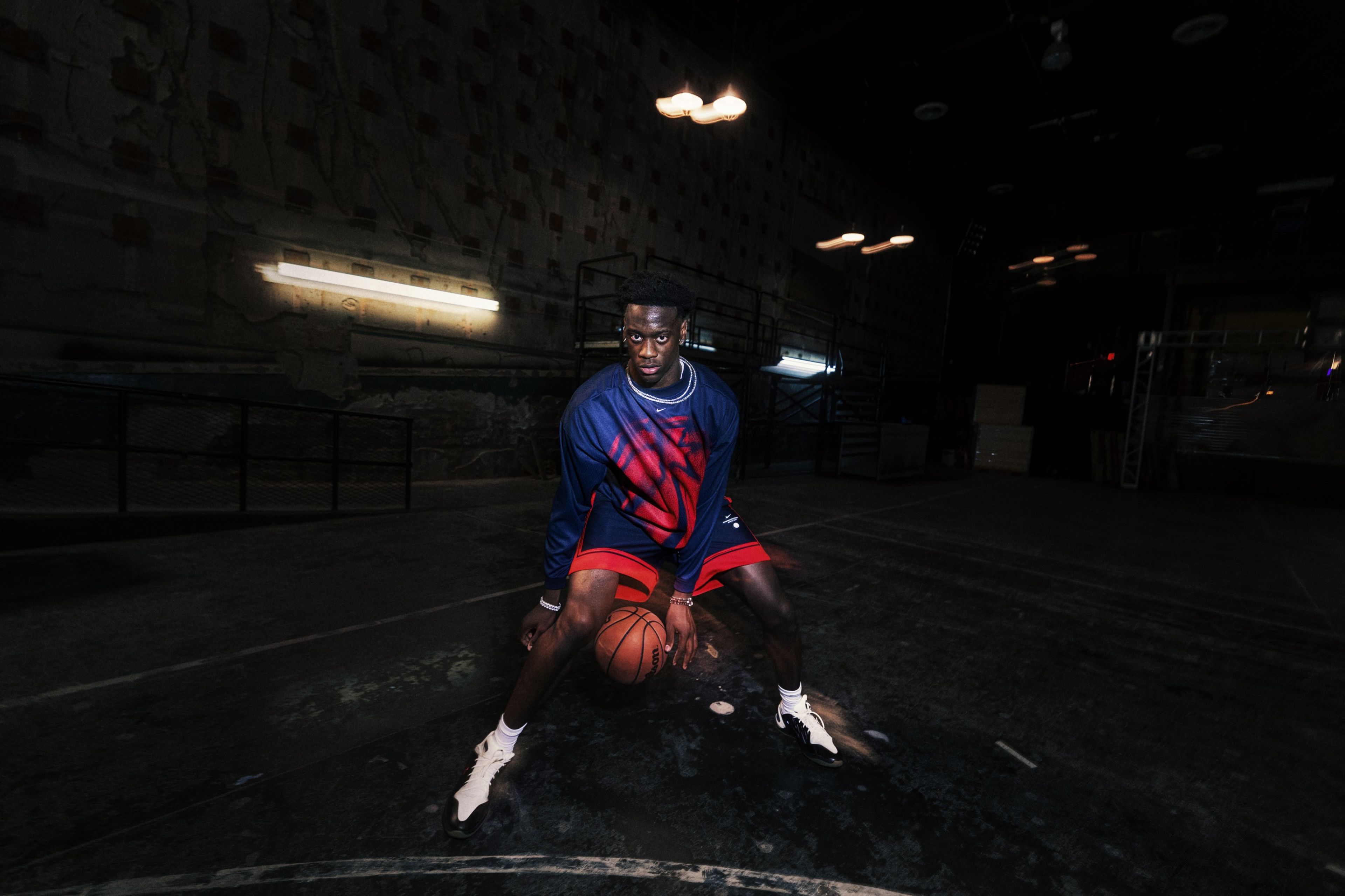 Nike athlete AJ Dybantsa dribbles a basketball between his legs while wearing pieces from Nike’s NBA Standard Issue Collection.