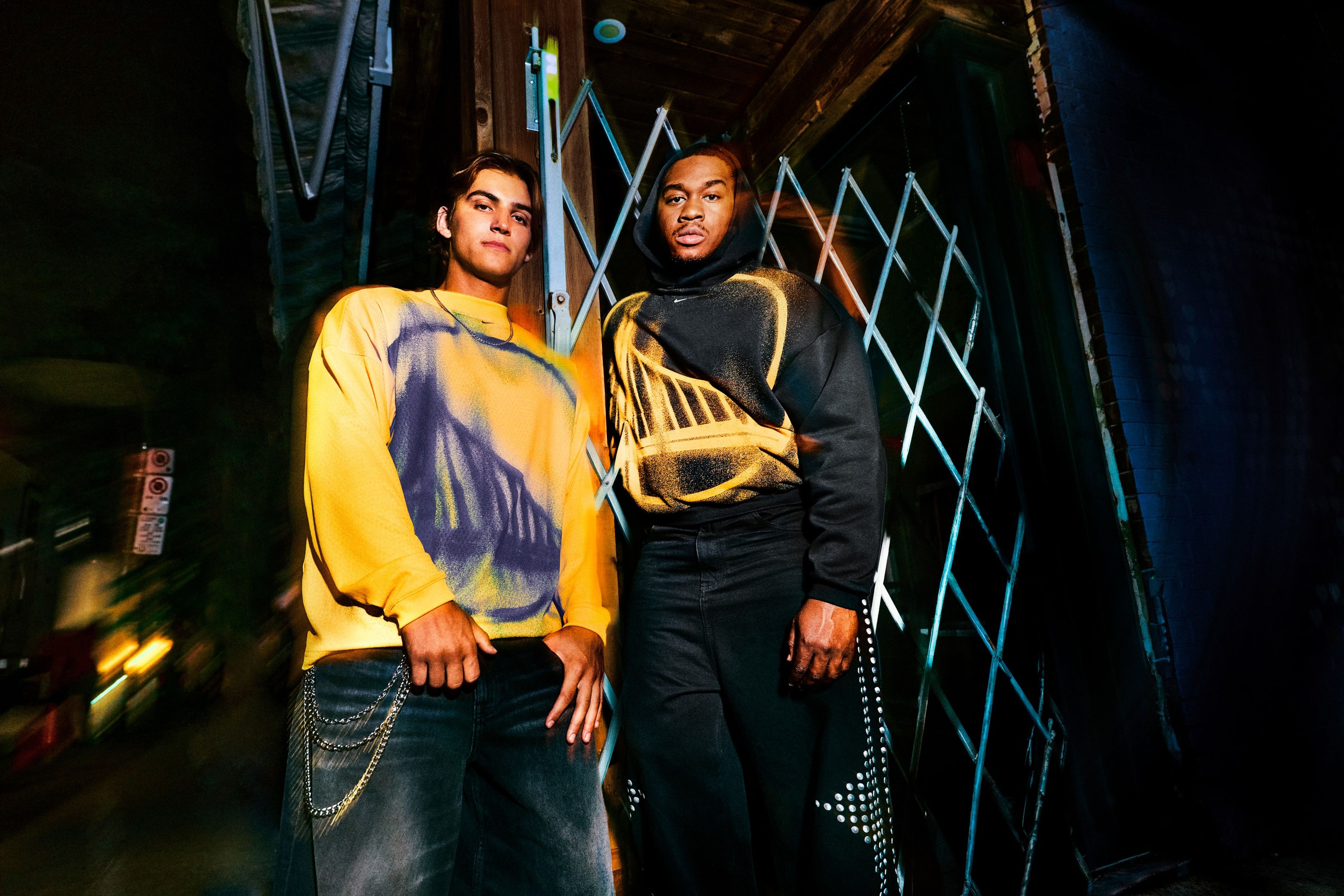 Two men pose for a photo wearing yellow and black Golden State Warriors pieces from Nike’s NBA Standard Issue Collection. The yellow piece has a blue Warriors logo.